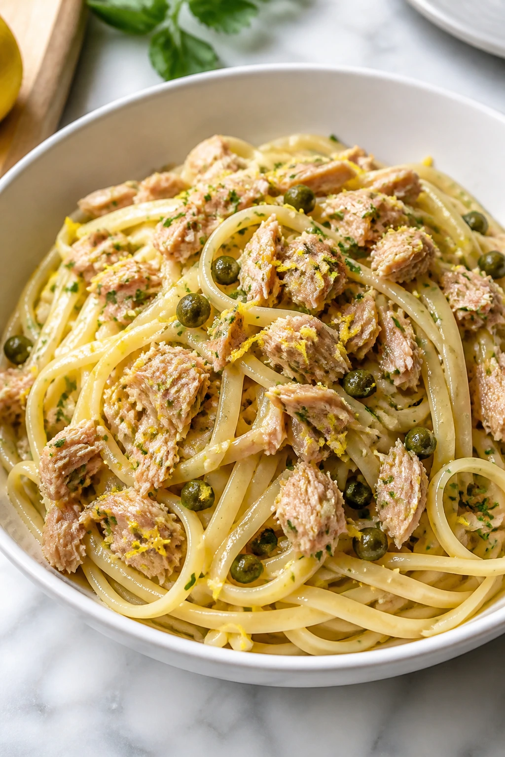 Bright lemon tuna pasta with capers in a bowl on a kitchen counter.