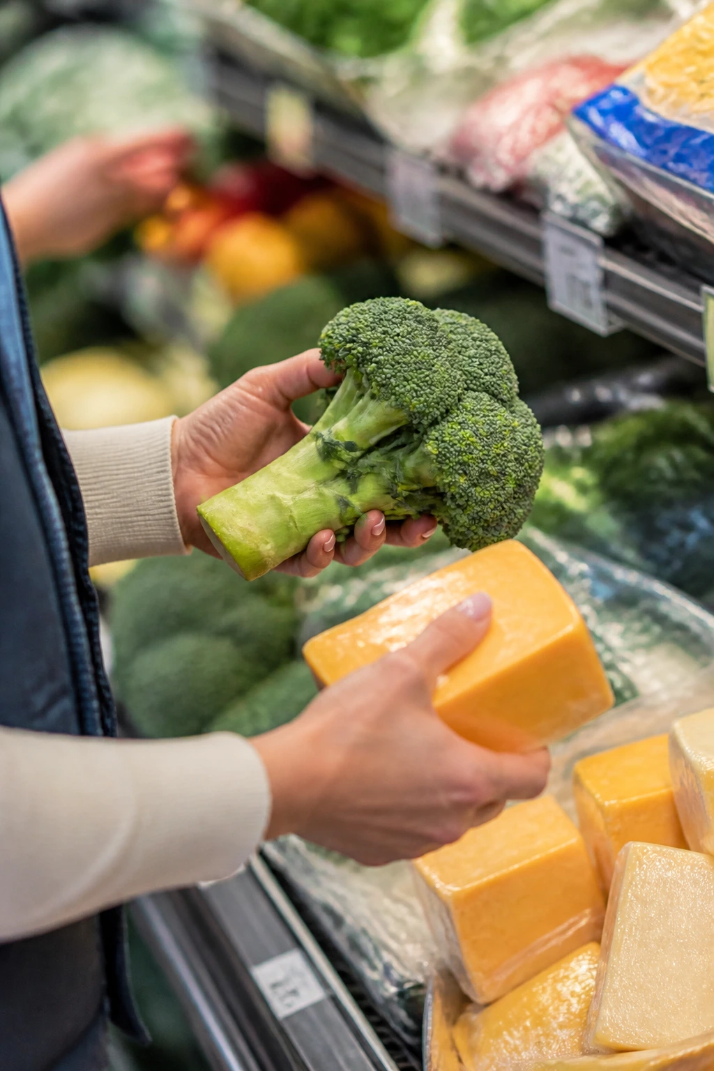 Hands selecting broccoli and cheese in a grocery store