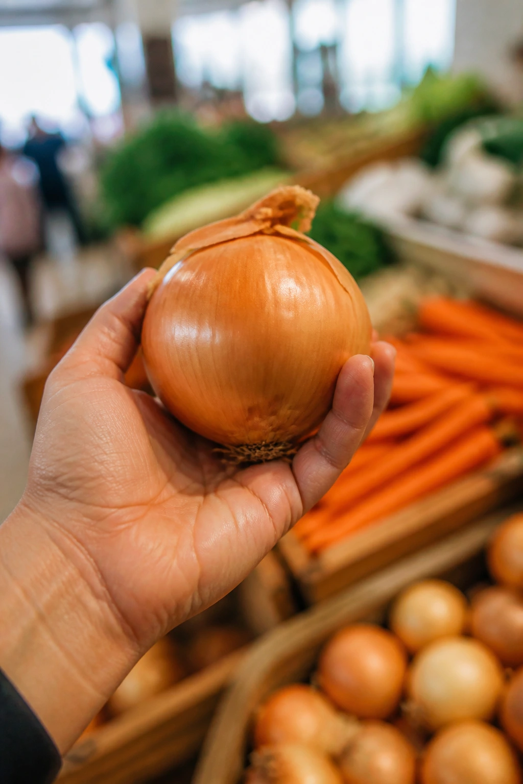 Hand holding onion in market setting with blurred produce stalls