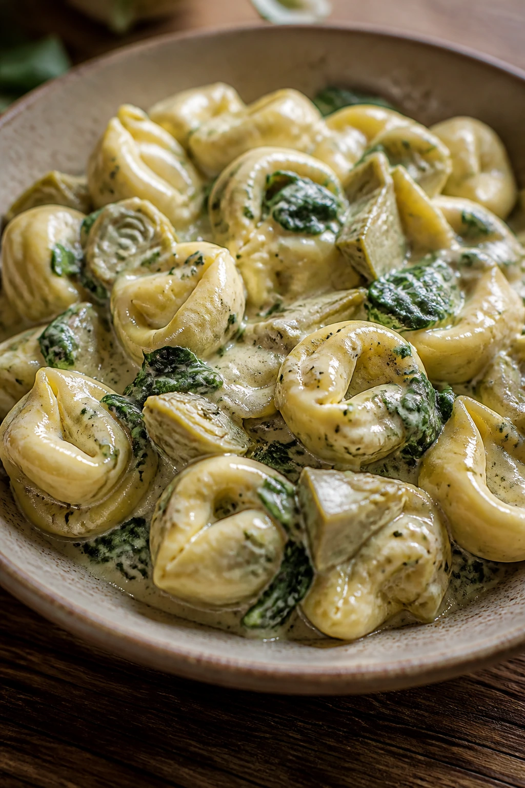 Close-up of spinach artichoke tortellini in creamy sauce on a rustic plate
