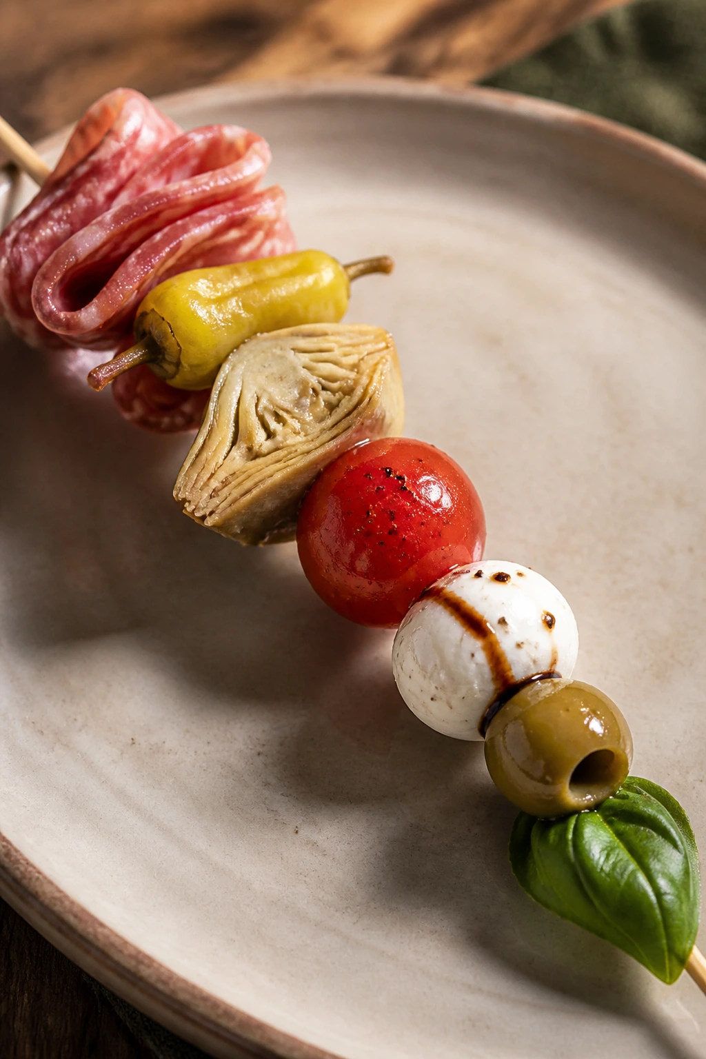Antipasto caprese skewers with salami, olives, pepperoncini, artichokes, tomato, mozzarella, and basil on a rustic table