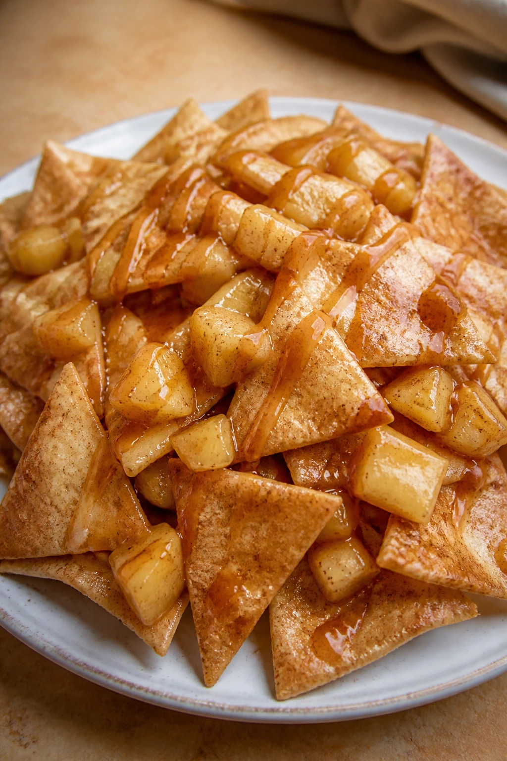 Plate of apple pie nachos with spiced apples and caramel on a warm surface