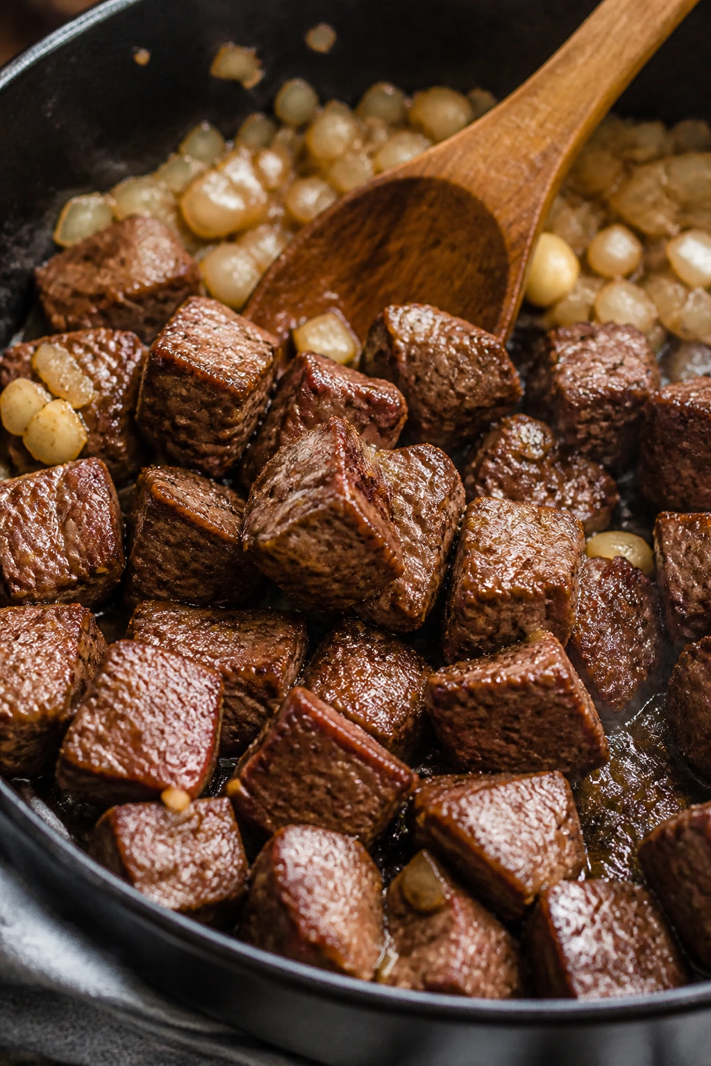 Browned beef cubes in a skillet with onions and garlic ready to build the stew