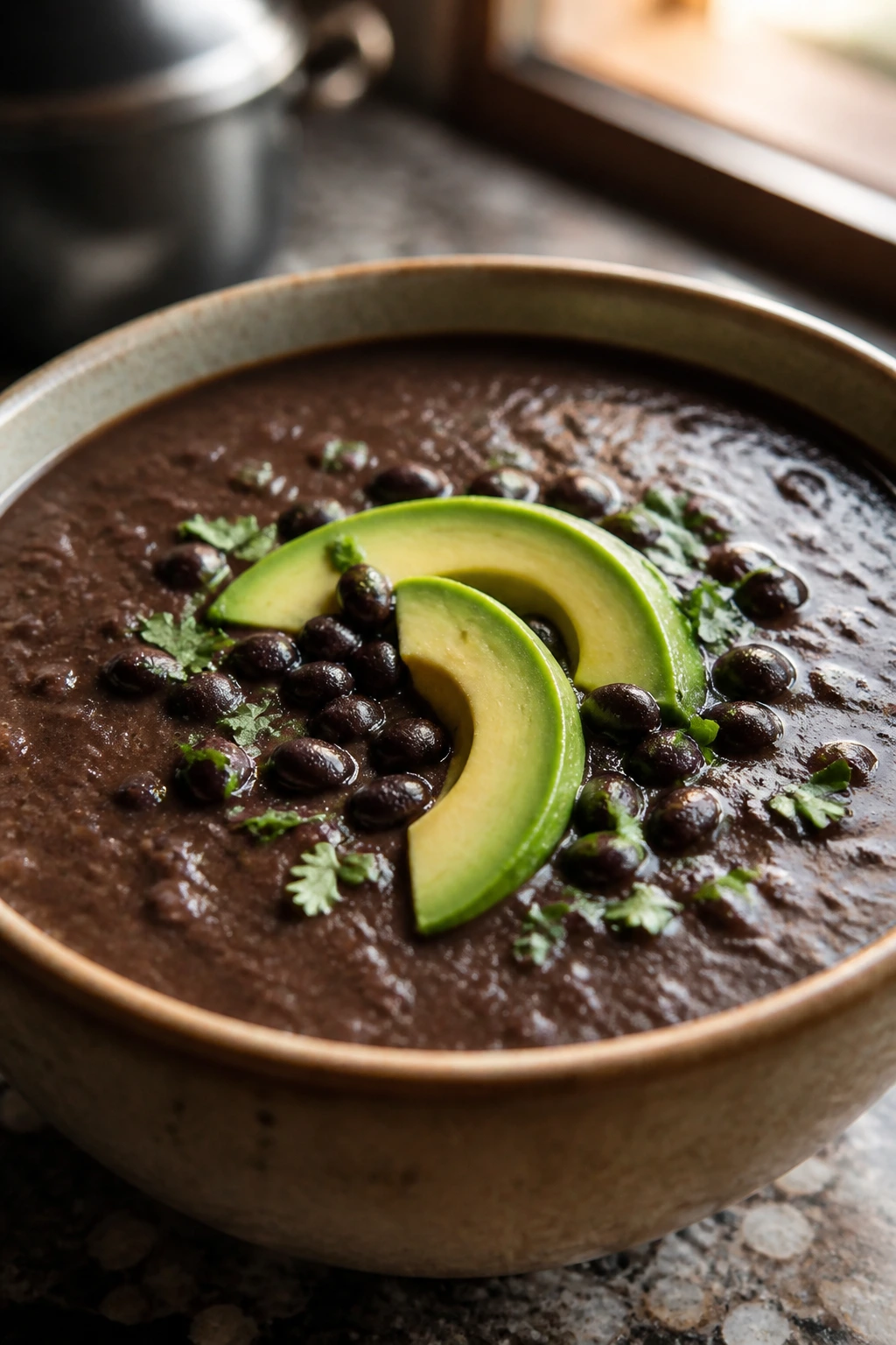 Bowl of black bean soup with avocado garnish on a warm kitchen counter