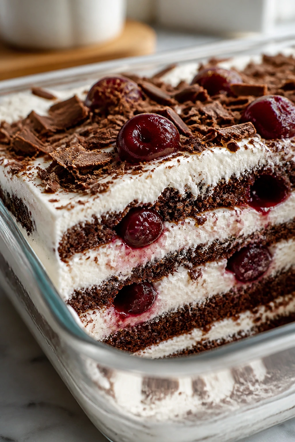 Layered no-bake Black Forest cake slice in a glass dish showing cookies, cream, and cherries
