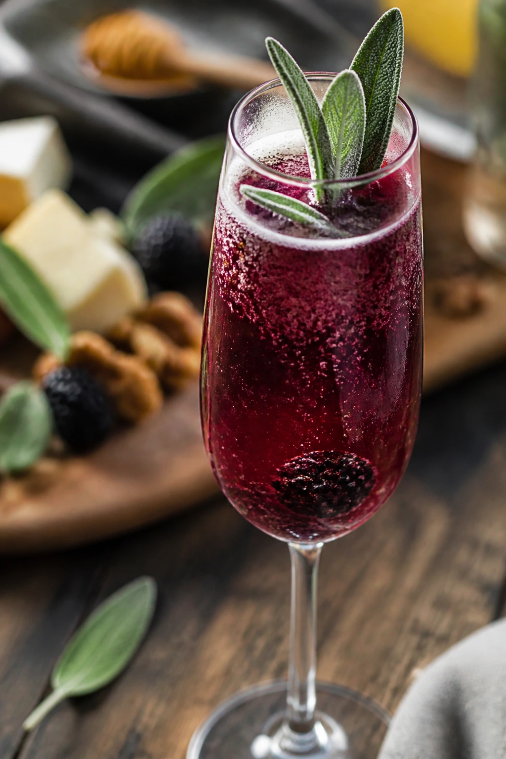 Close-up of Blackberry Sage Sparkle flute with blackberry and sage garnish on a rustic brunch table