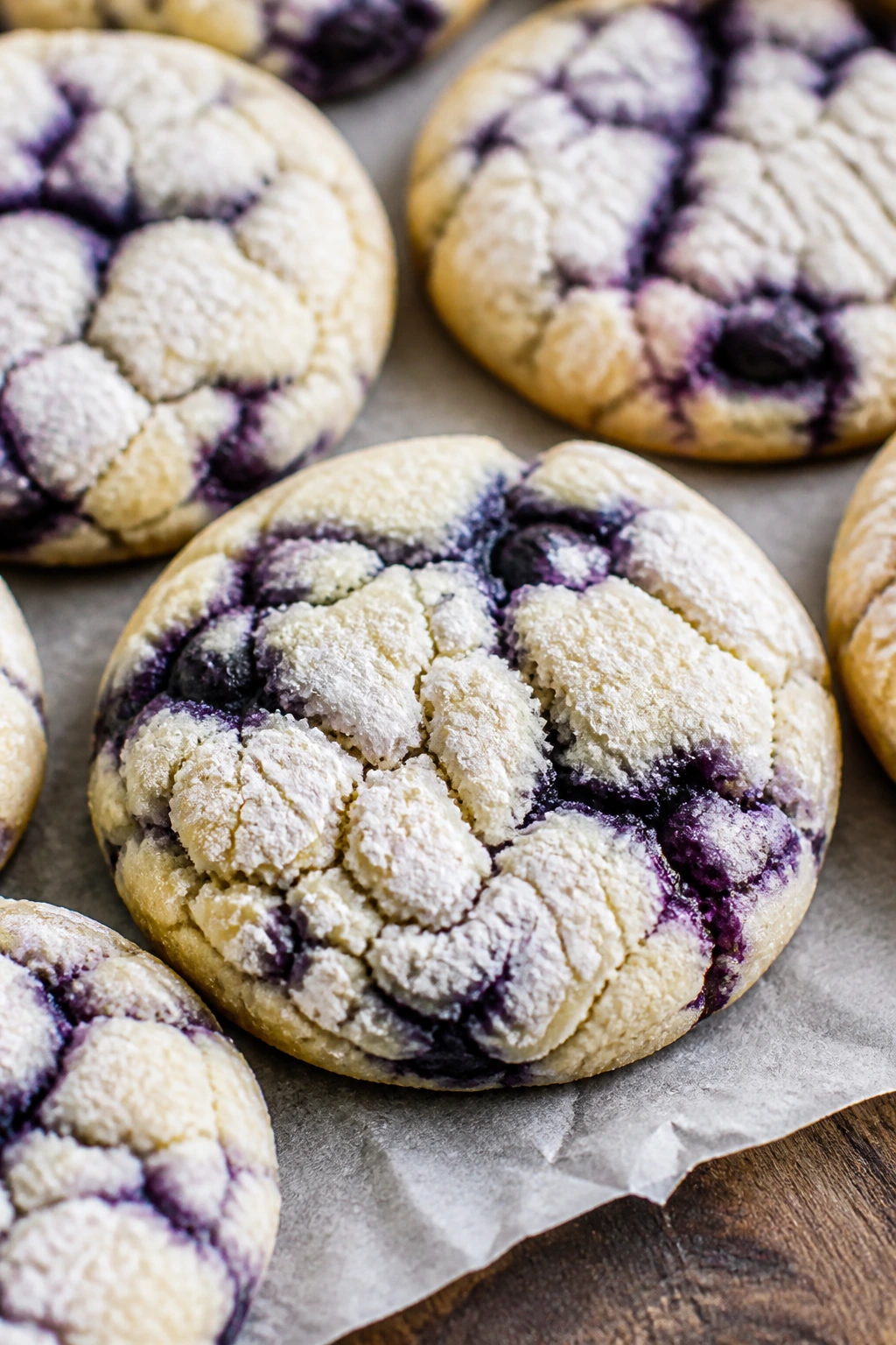 Close-up of pale blueberry lemon crinkle cookies with blue streaks on a rustic wooden surface