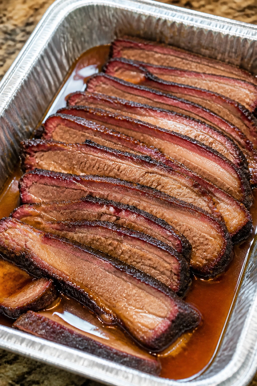 Brisket slices in foil pan with broth for reheating