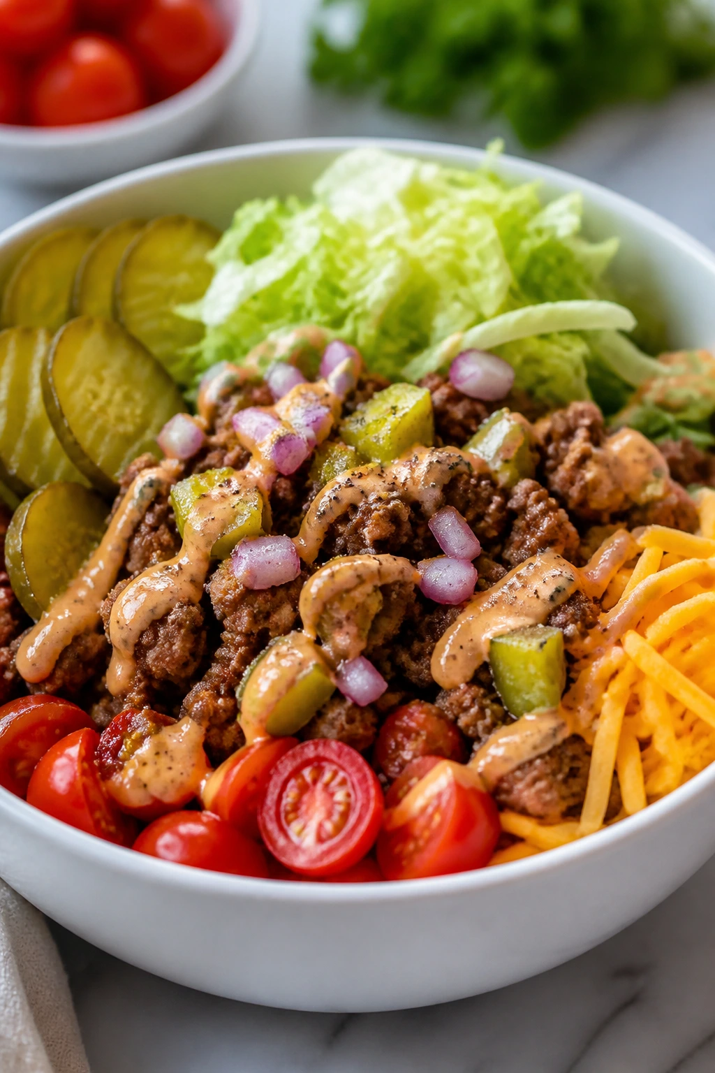 Close-up of a burger bowl with greens, tomatoes, pickles, and creamy sauce on a kitchen counter