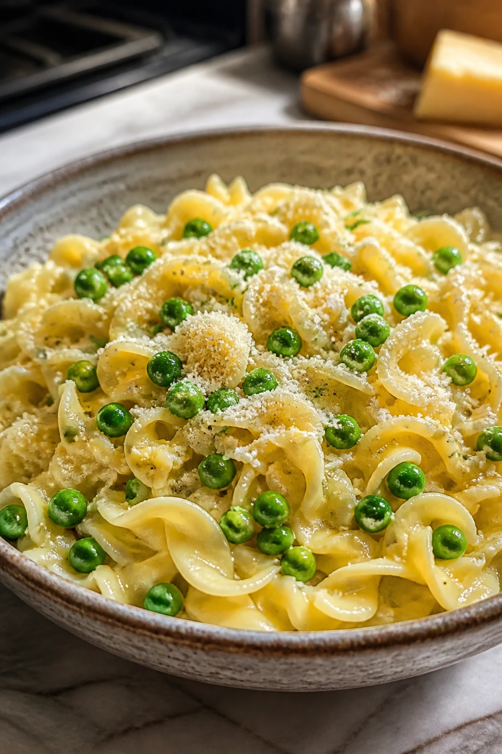 Close-up of buttered noodles with peas and parmesan in a rustic bowl on a kitchen counter