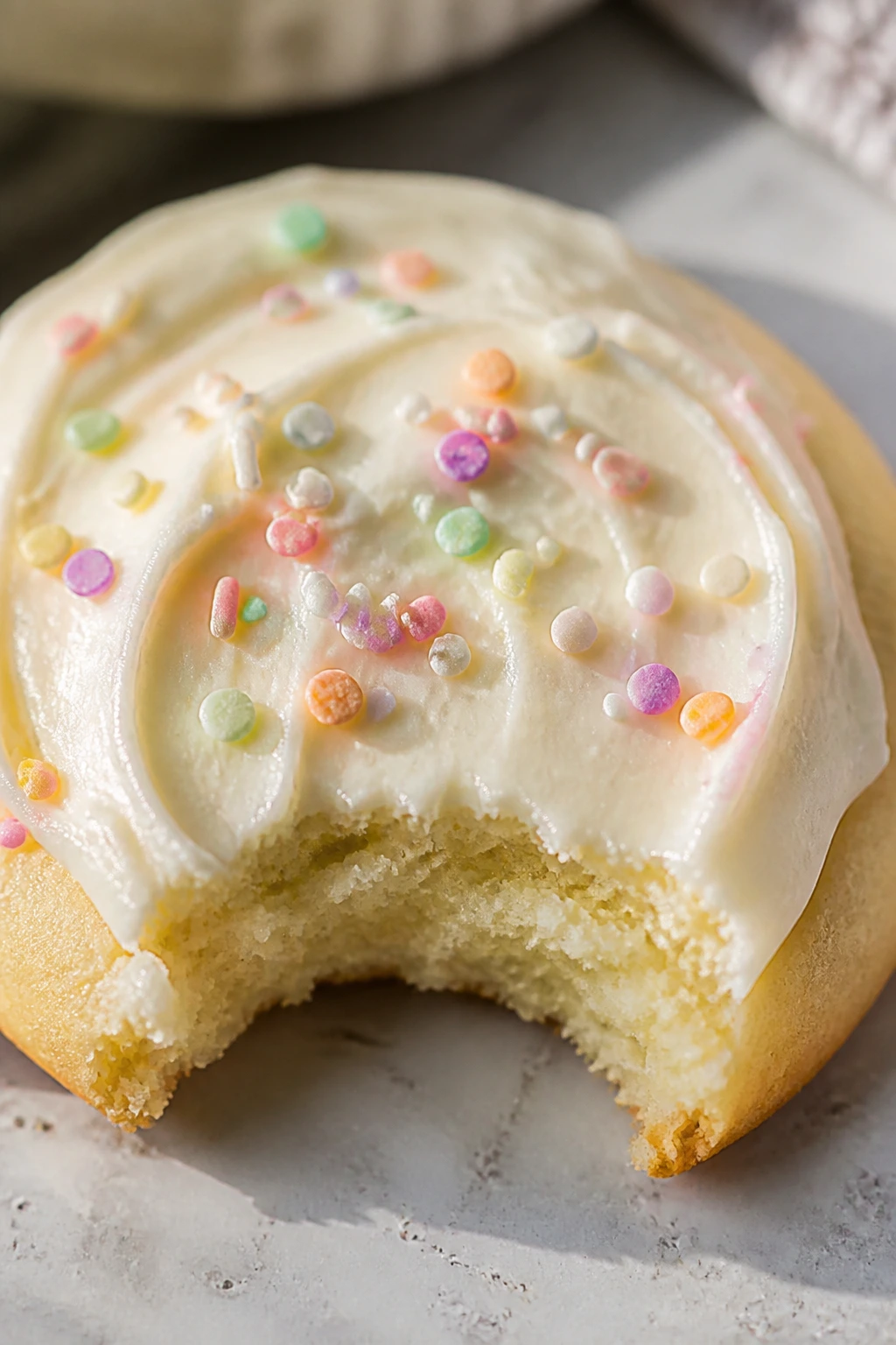 Close-up of a single pale-yellow Easter cookie with cream cheese frosting on a kitchen counter