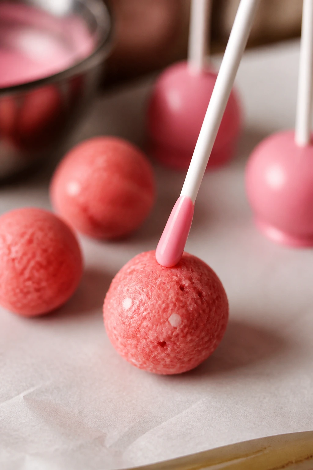 Close-up of a pink cake pop with dipped stick tip ready to insert into the ball.