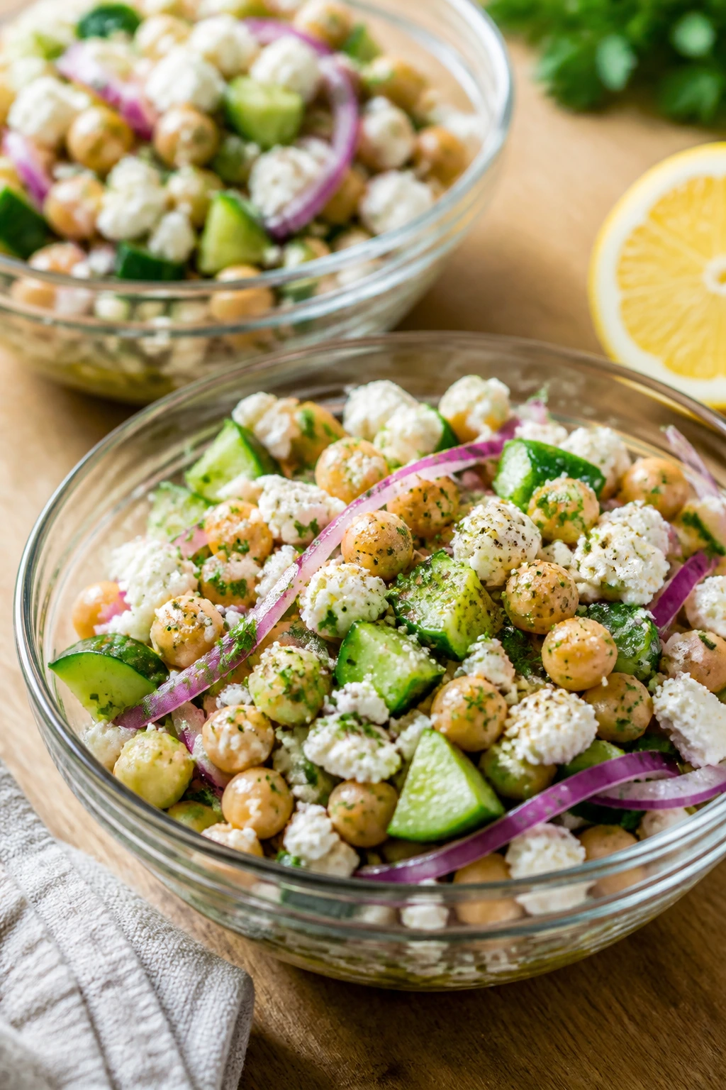Two bowls of Greek chickpea cucumber salad with feta and lemon dressing on a light wooden table