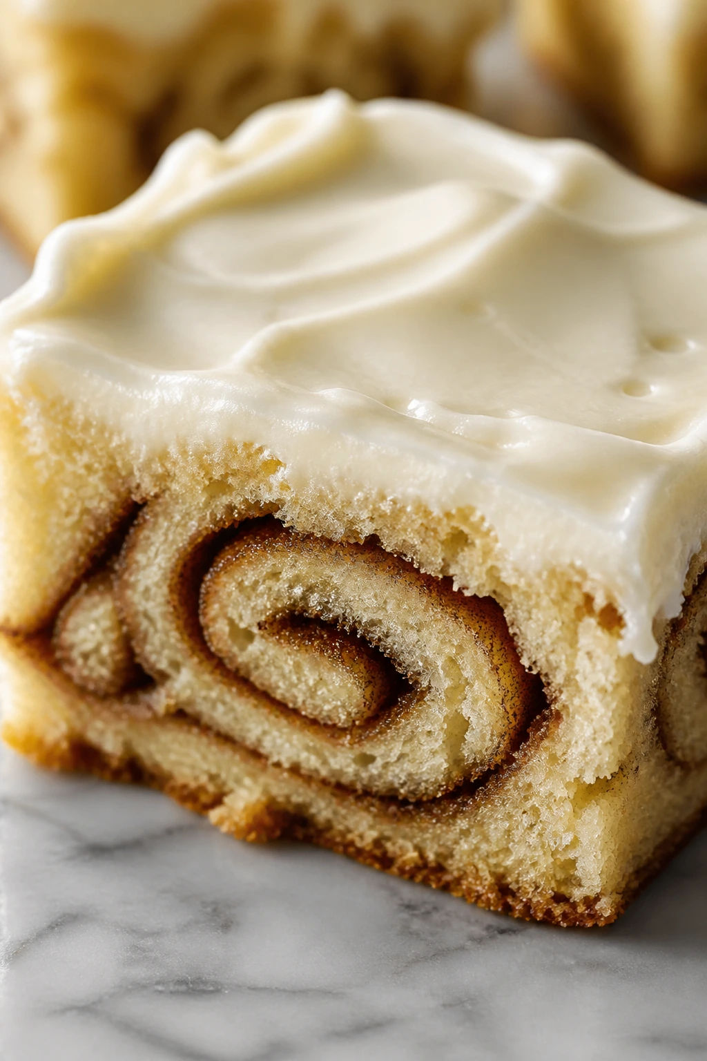 Close-up of a cinnamon swirl bar topped with cream cheese frosting on a kitchen counter