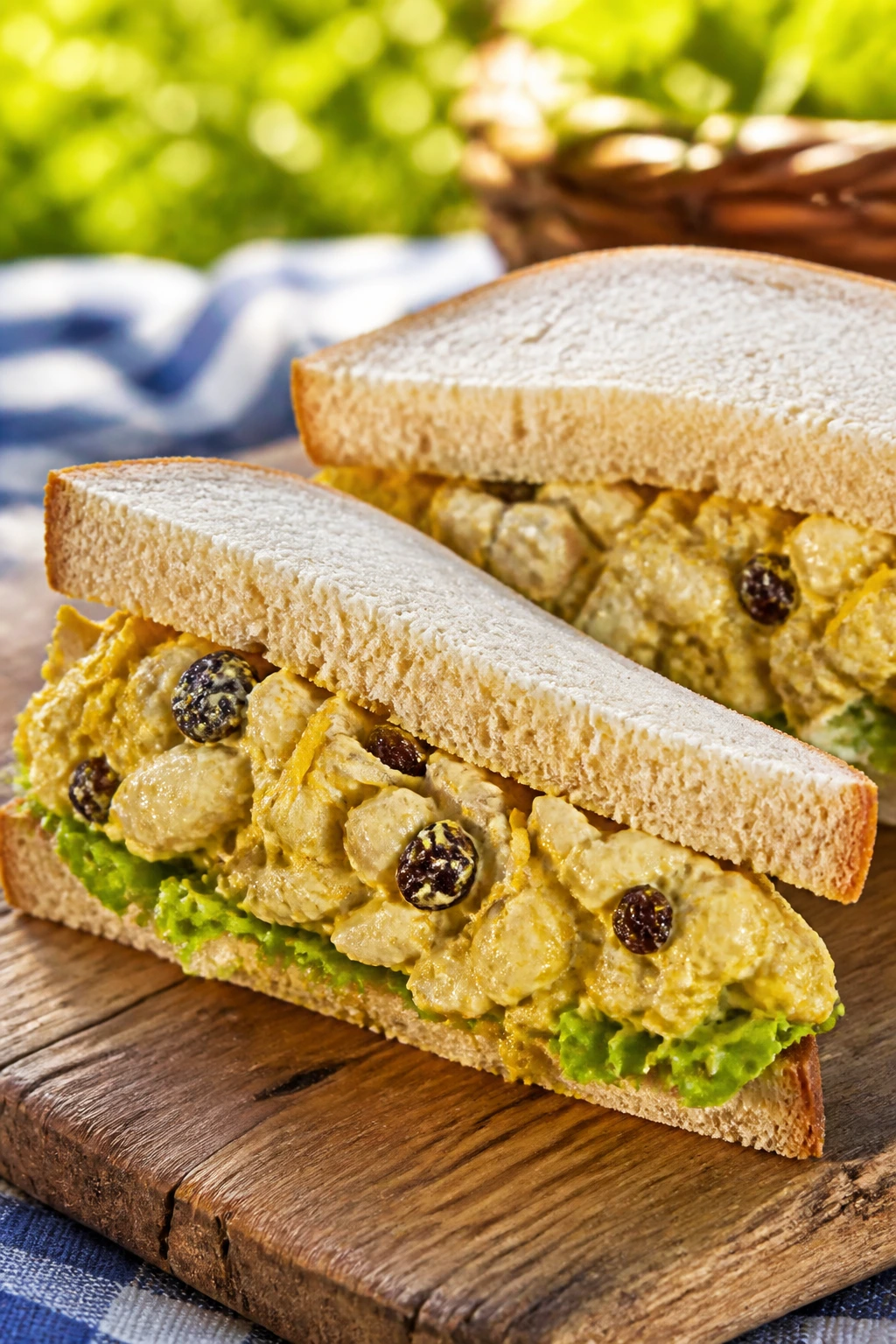 Close-up of coronation chicken sandwich with curry filling and lettuce on a rustic wooden board outdoors.