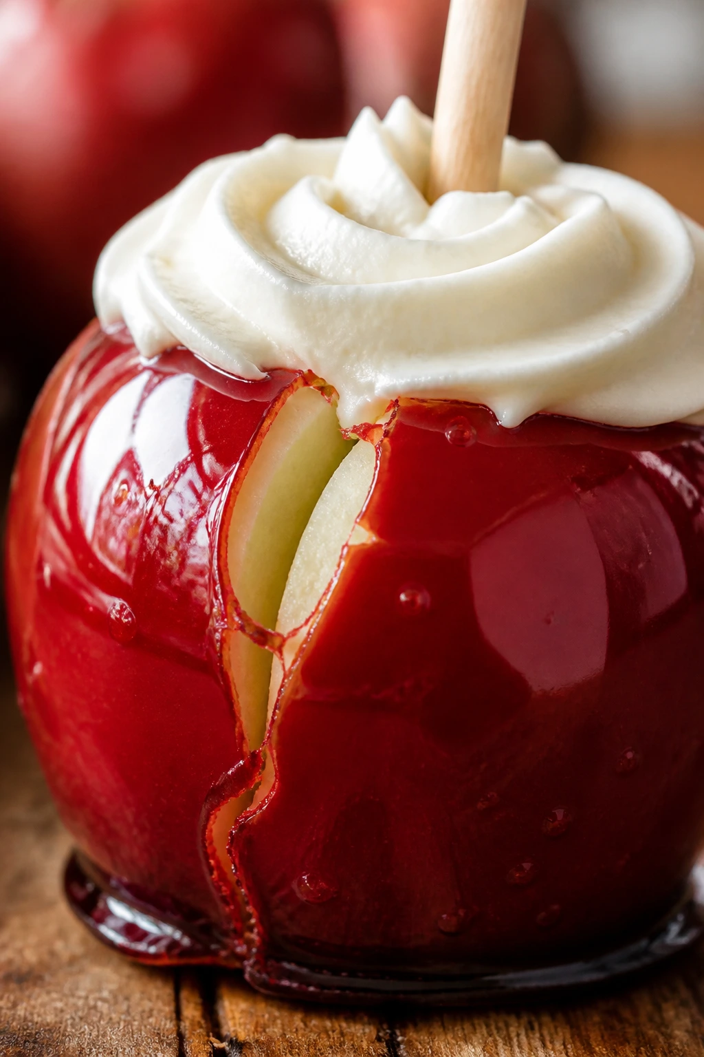 Close-up of a glossy candy-coated apple with a visible shell crack and a cream cheese frosting crown