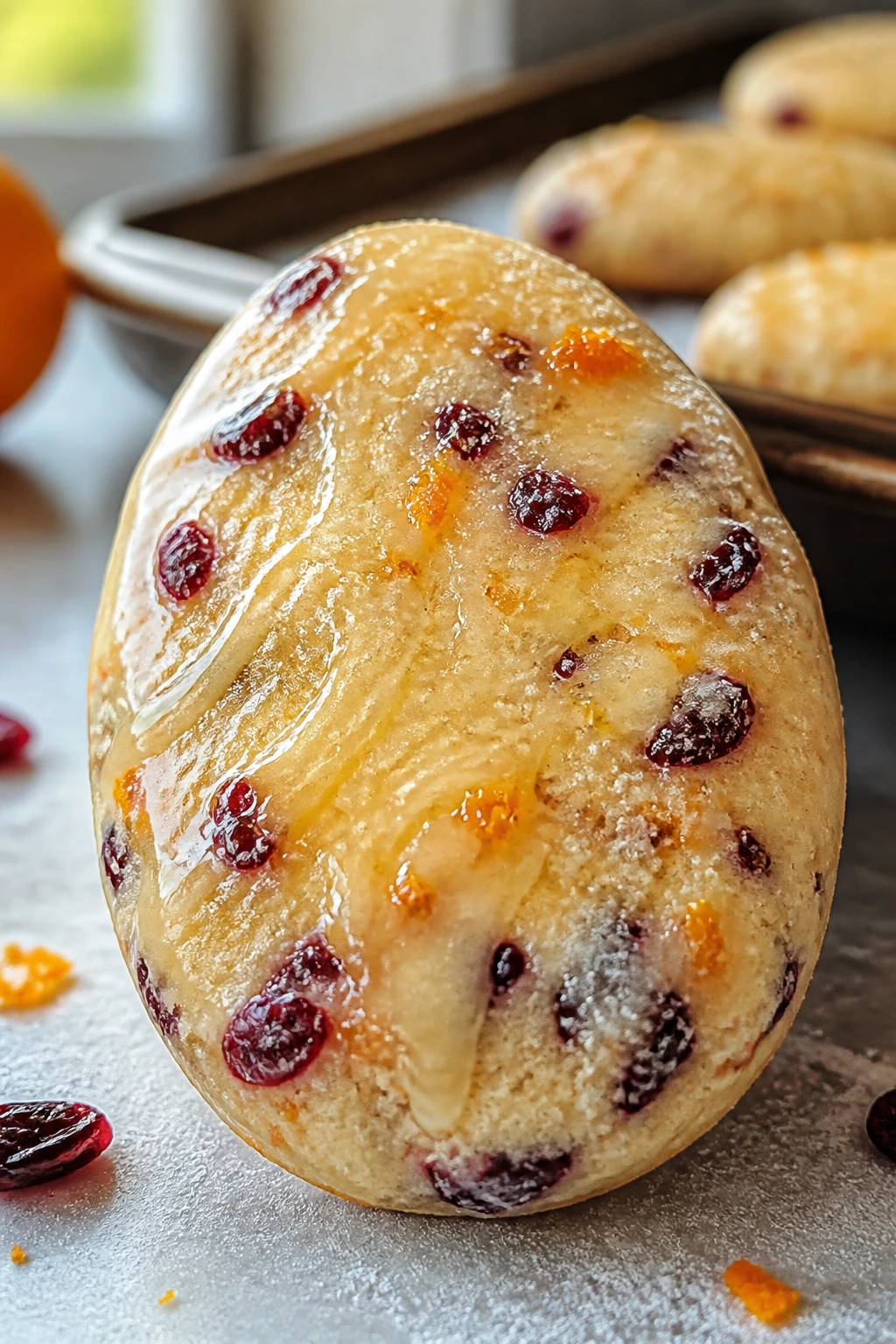 Close-up of cranberry studded Easter egg cookie with orange glaze on counter