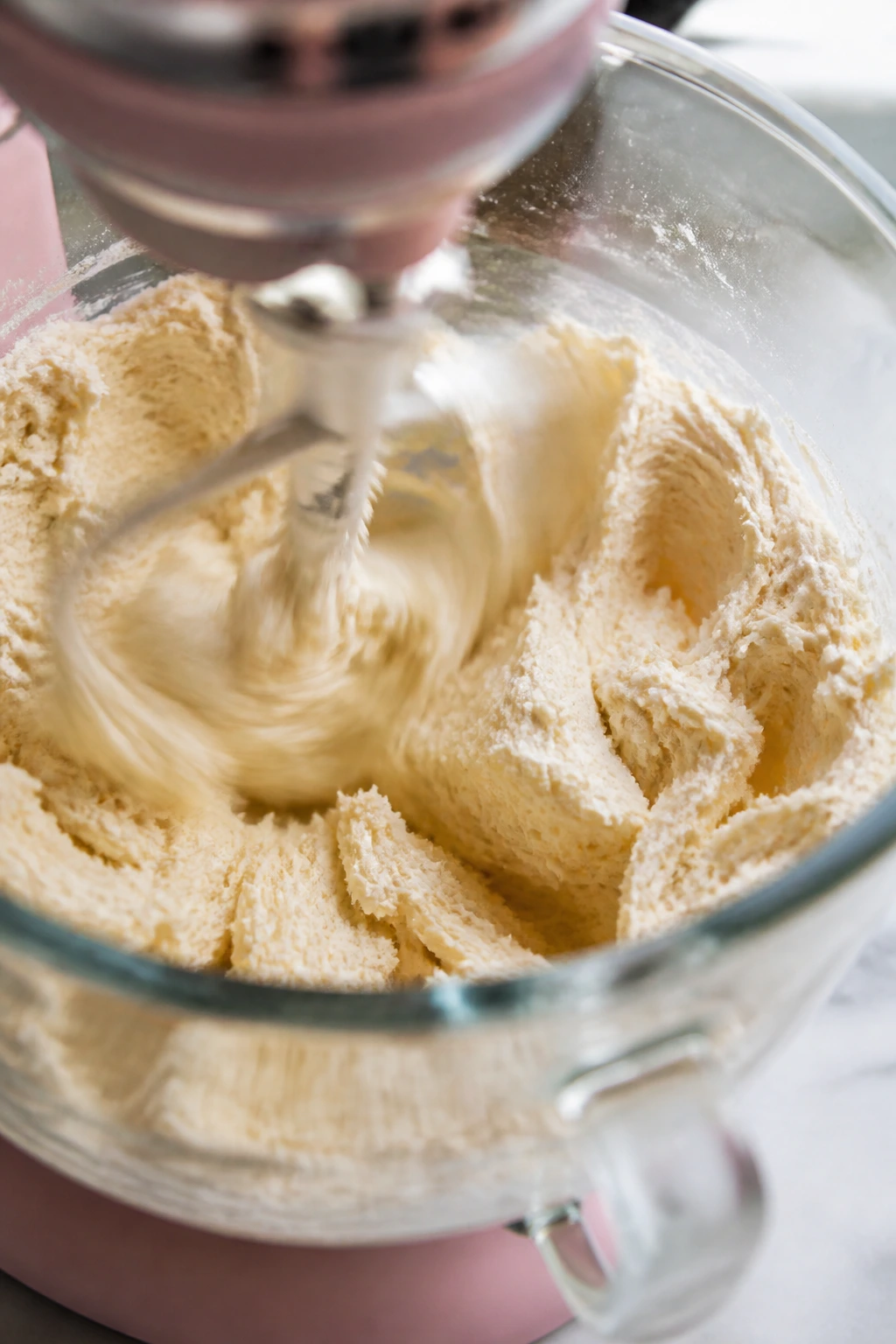 Close-up of a stand mixer bowl with pale cookie dough being creamed.