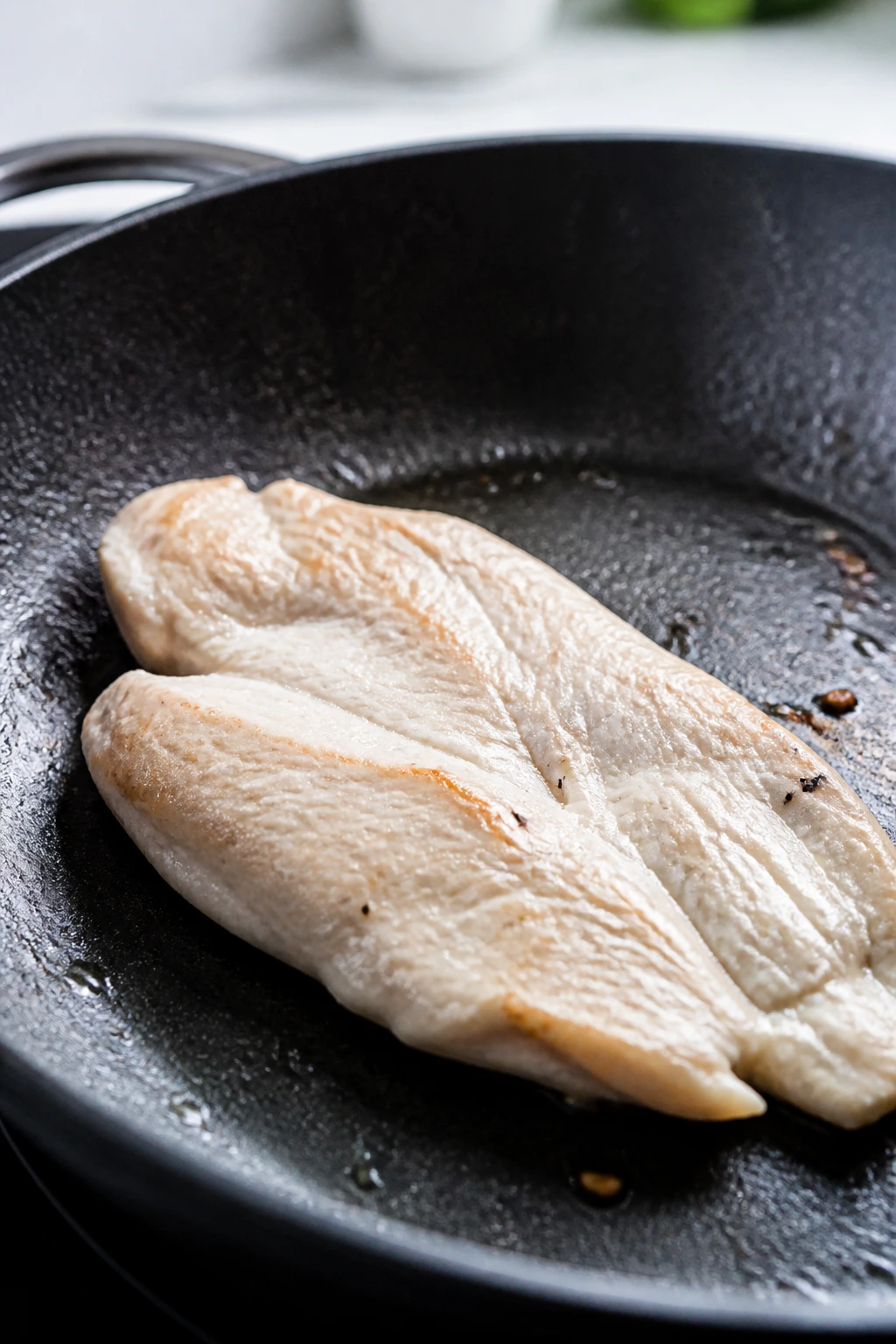 Close-up of a pale dry chicken cutlet in a pan, showing bad searing.