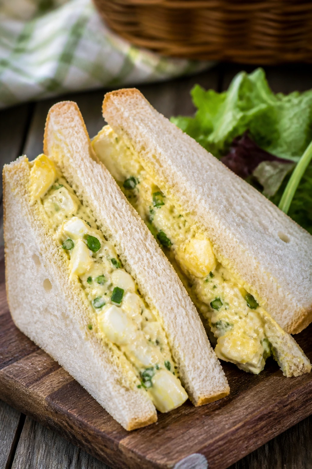 Egg salad sandwiches with chives on soft bread, outdoors on a picnic table