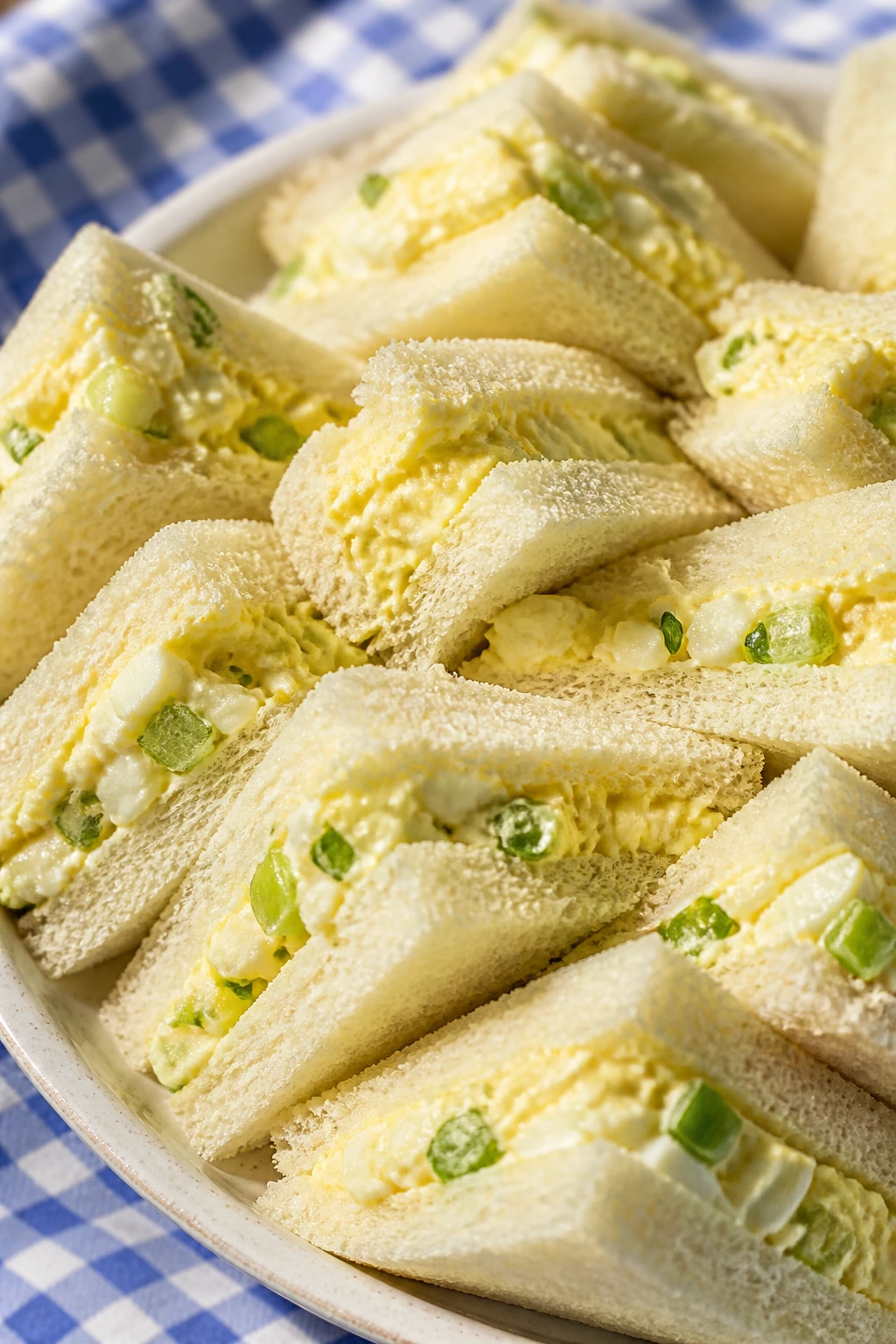 Egg salad tea sandwiches on a plate at a sunlit picnic setting