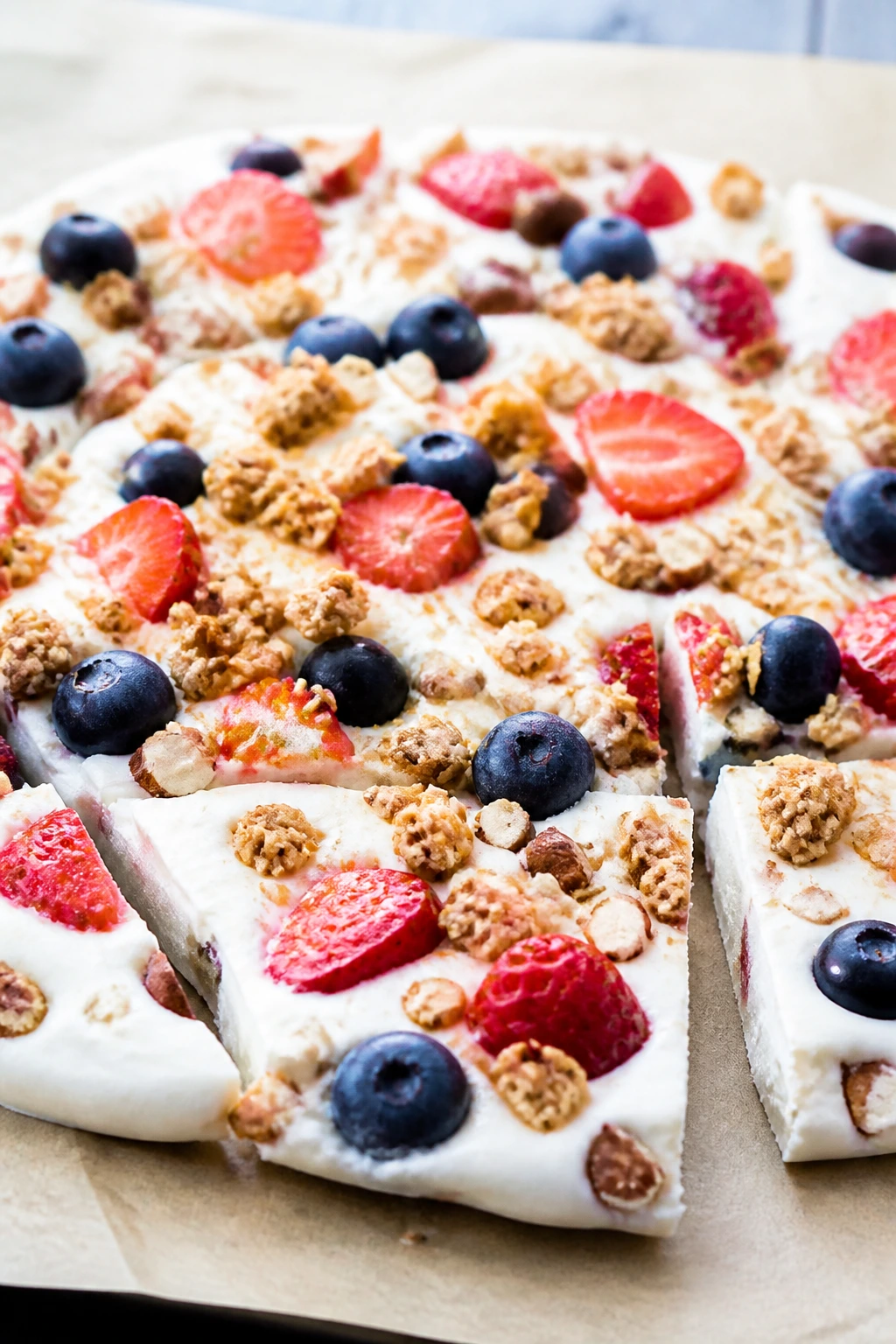 Close-up of frozen yogurt bark with berries and granola on parchment in a bright kitchen.