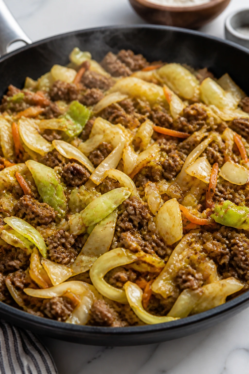 Beef and cabbage stir-fry in a skillet with steam