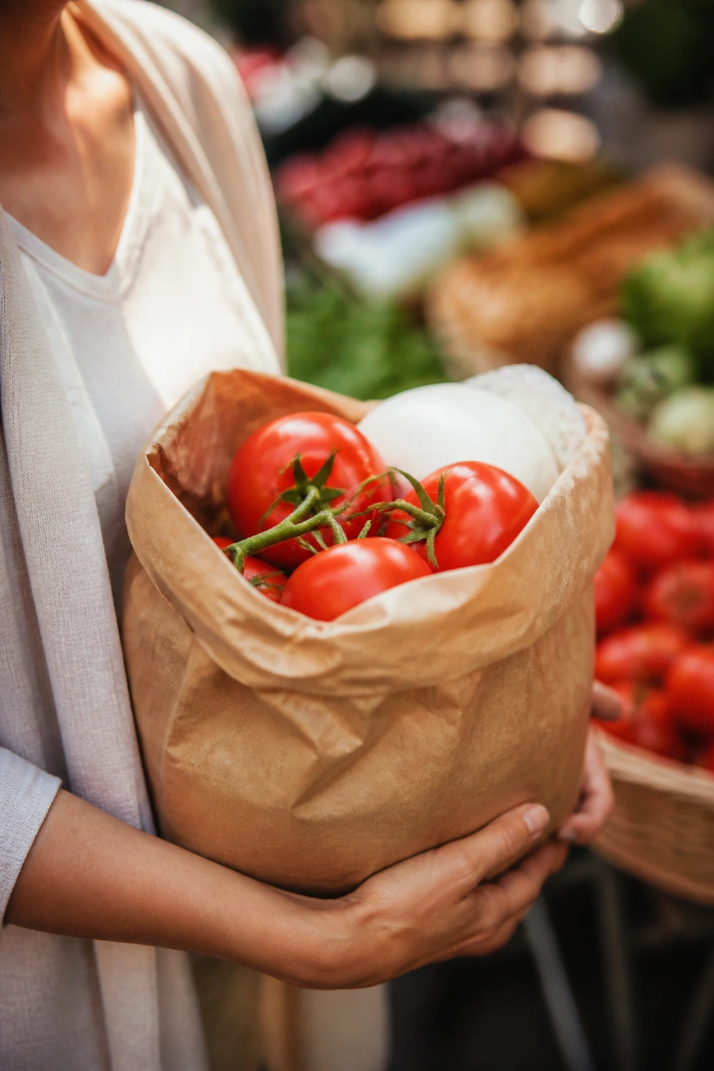 Close-up of a shopper's hands with a bag showing tomatoes and mozzarella in a market