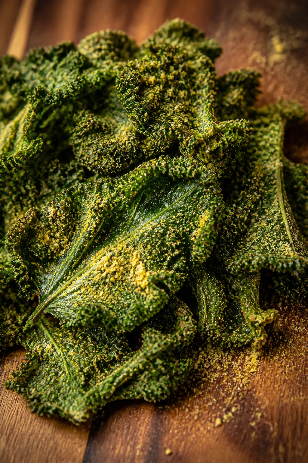 Close-up of crispy kale chips dusted with nutritional yeast on a dark wooden board