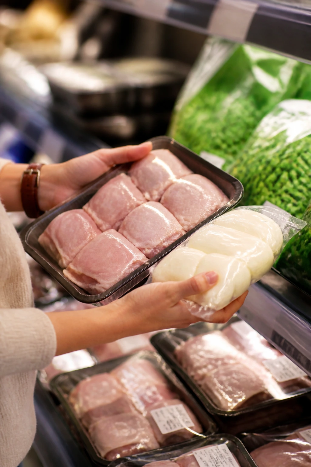 Hands selecting chicken thighs and mozzarella at a grocery store for kid-friendly meals.