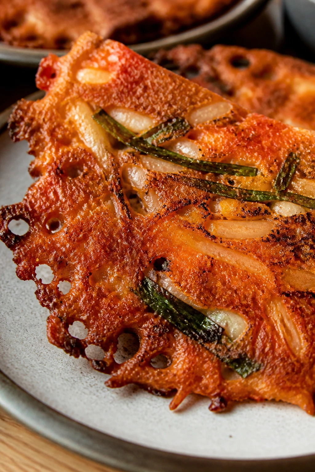 Crispy kimchi jeon slice with lacy edges on a plate.