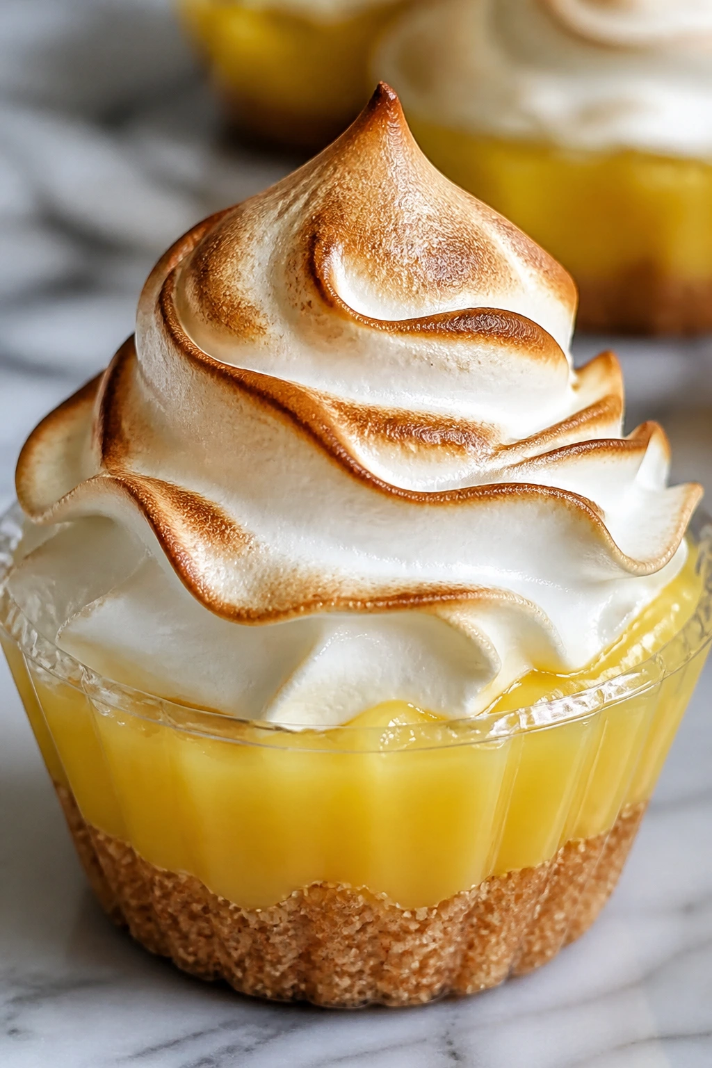 Close-up of a lemon meringue pie cup with tall meringue topping.