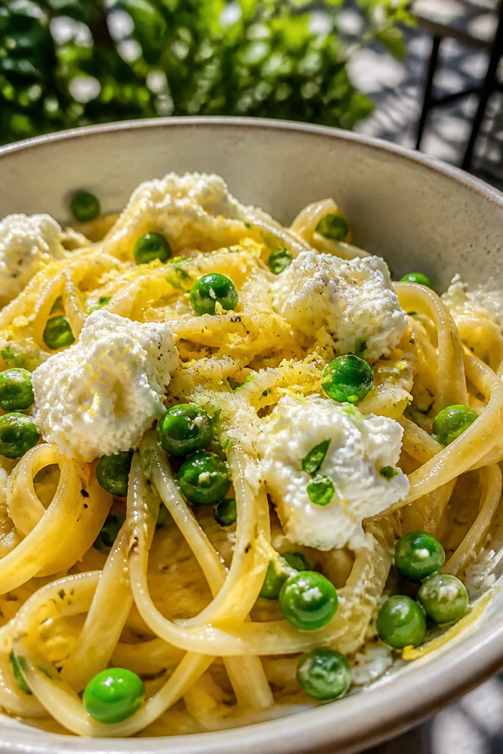 Bright lemon pasta with peas and ricotta in a bowl outdoors