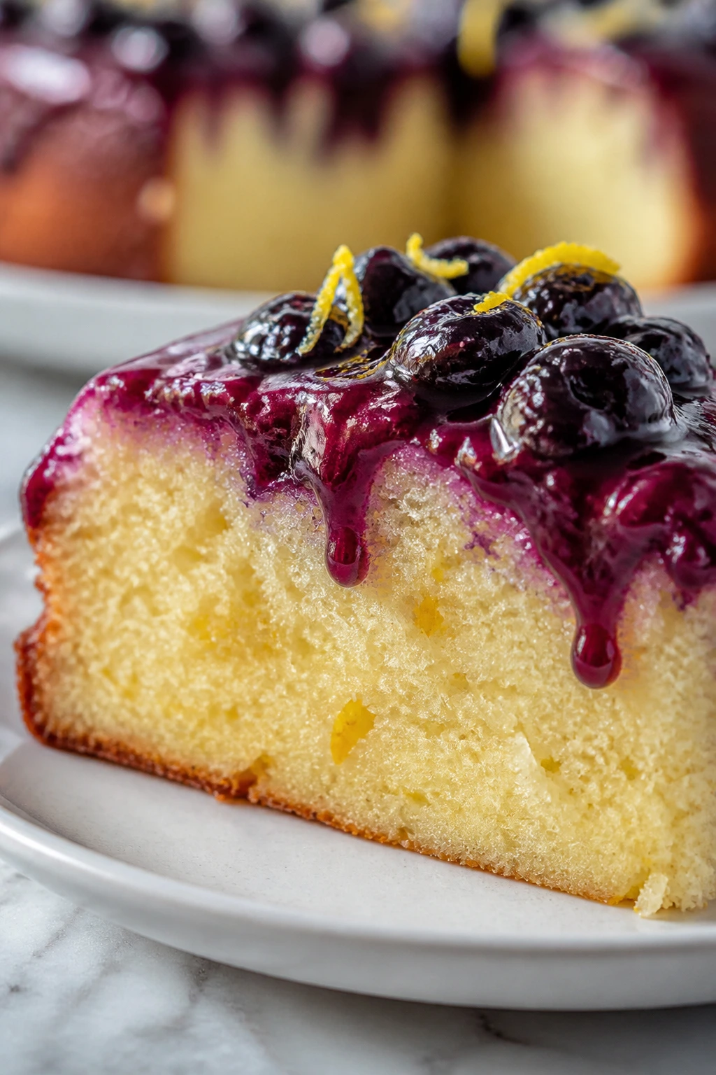 Slice of lemon ricotta olive oil cake with blueberry glaze and pale crumb