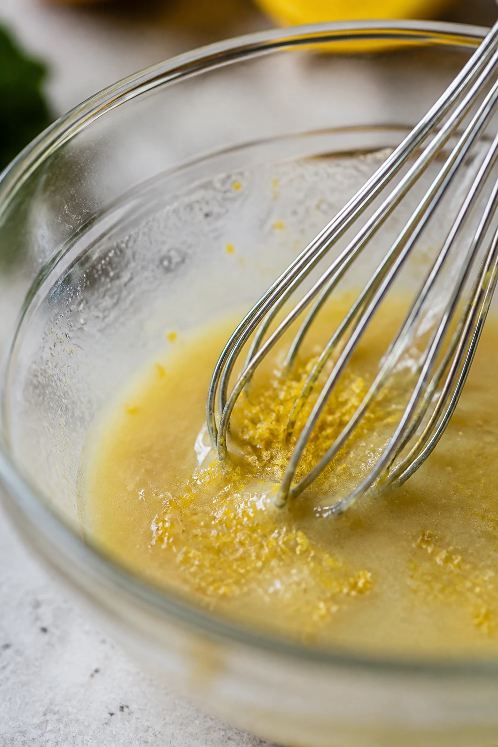Macro shot of lemon zest adding brightness to dressing in a glass bowl.