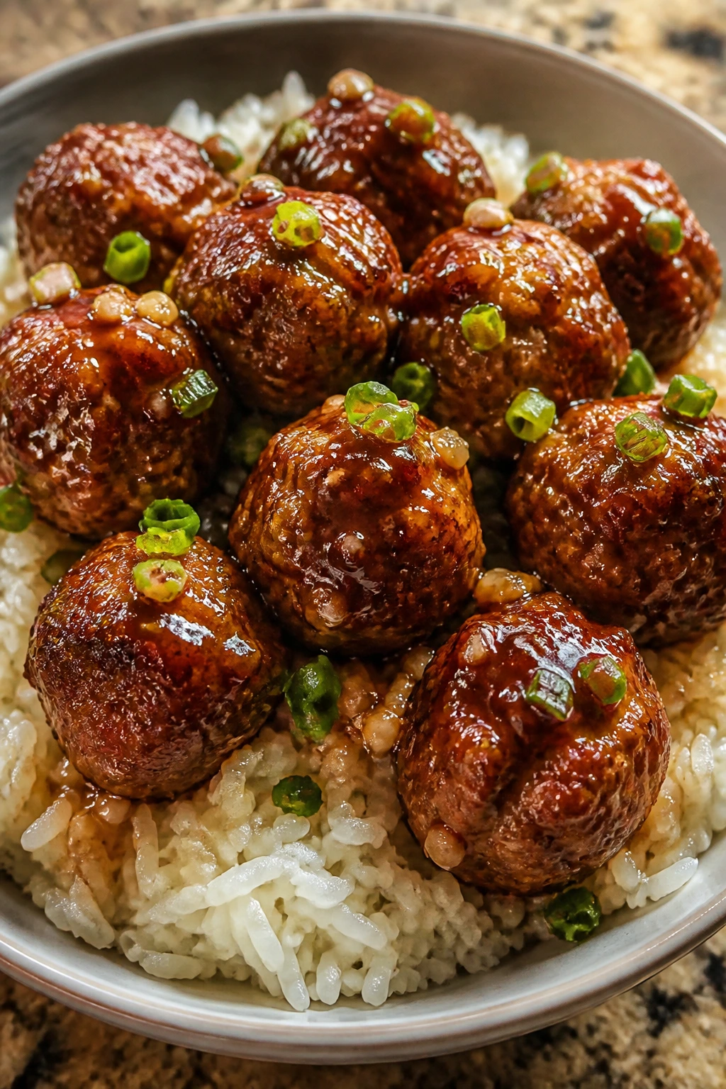 Glossy honey garlic meatballs over rice in a bowl.