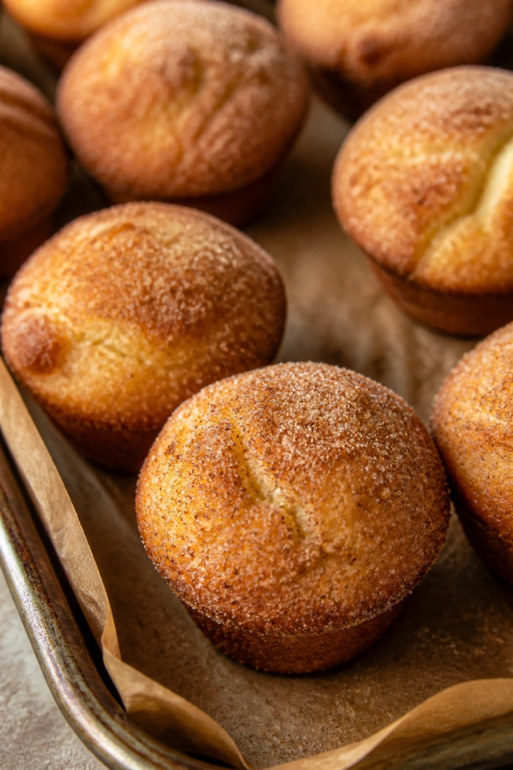 Close-up of golden mini muffins with cinnamon sugar on a baking sheet in a cozy kitchen