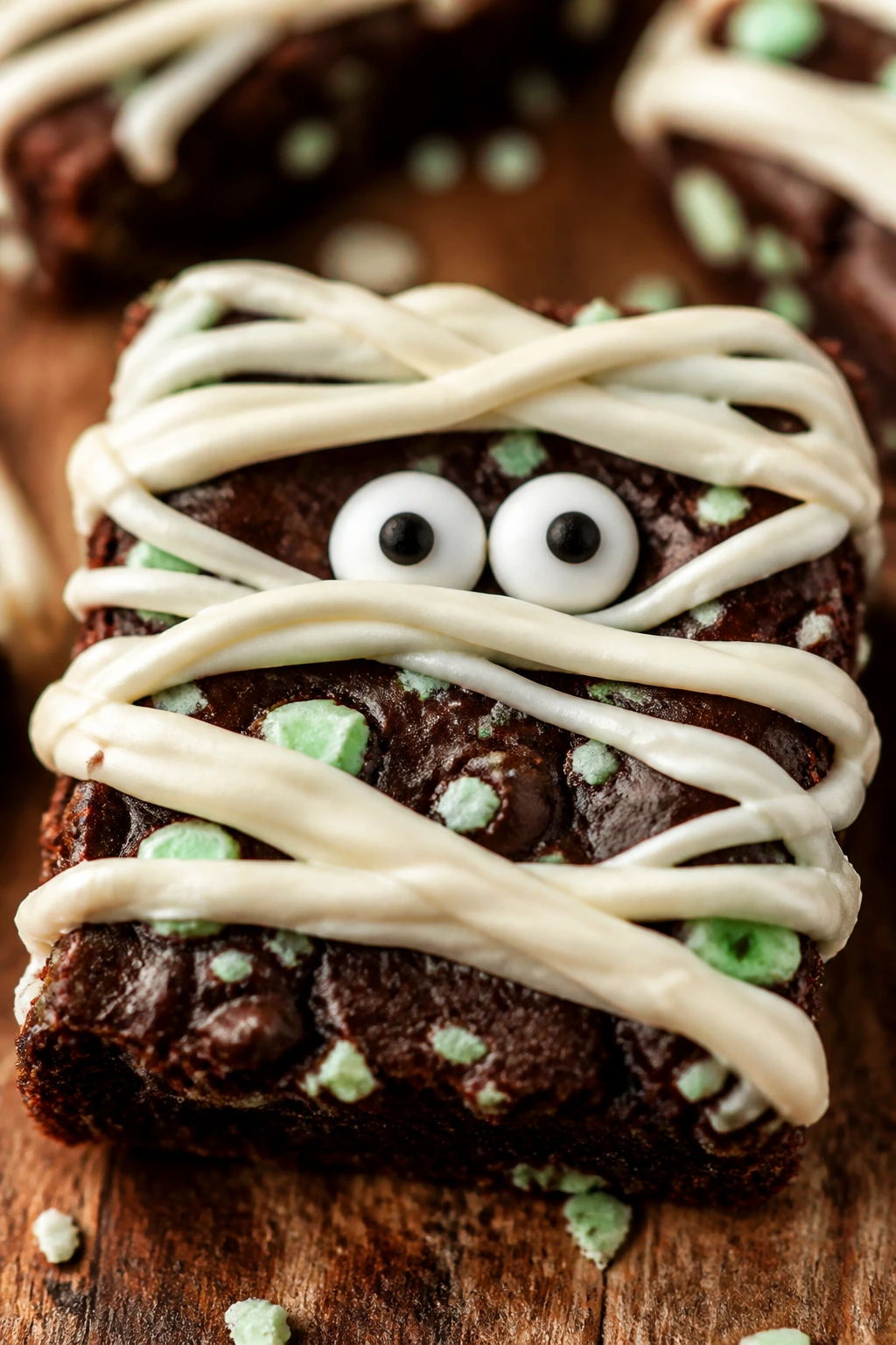 Close-up of a mint chocolate mummy brownie with candy eyes on a wooden surface