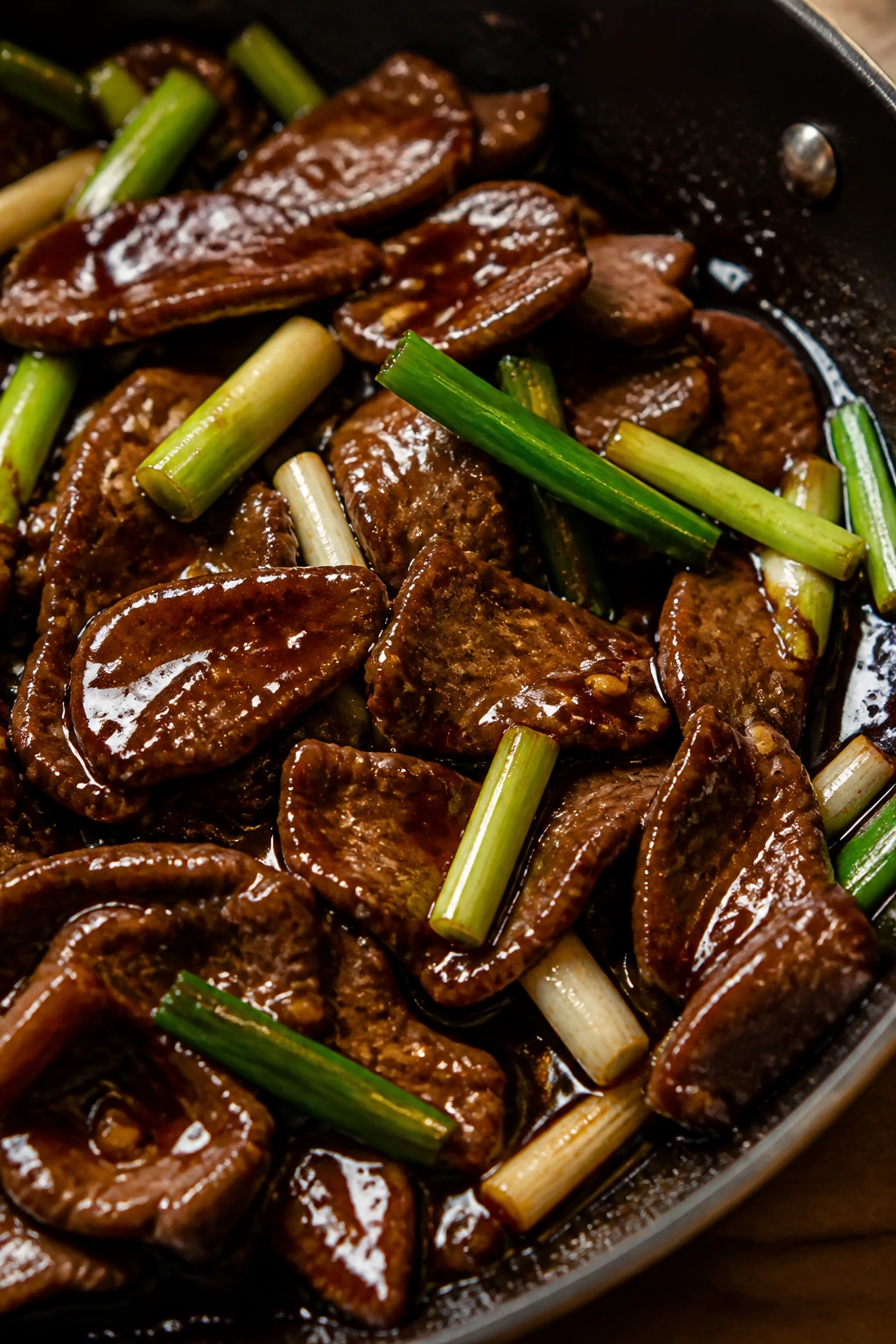 Close-up of Mongolian Beef with glossy sauce and scallions in a pan