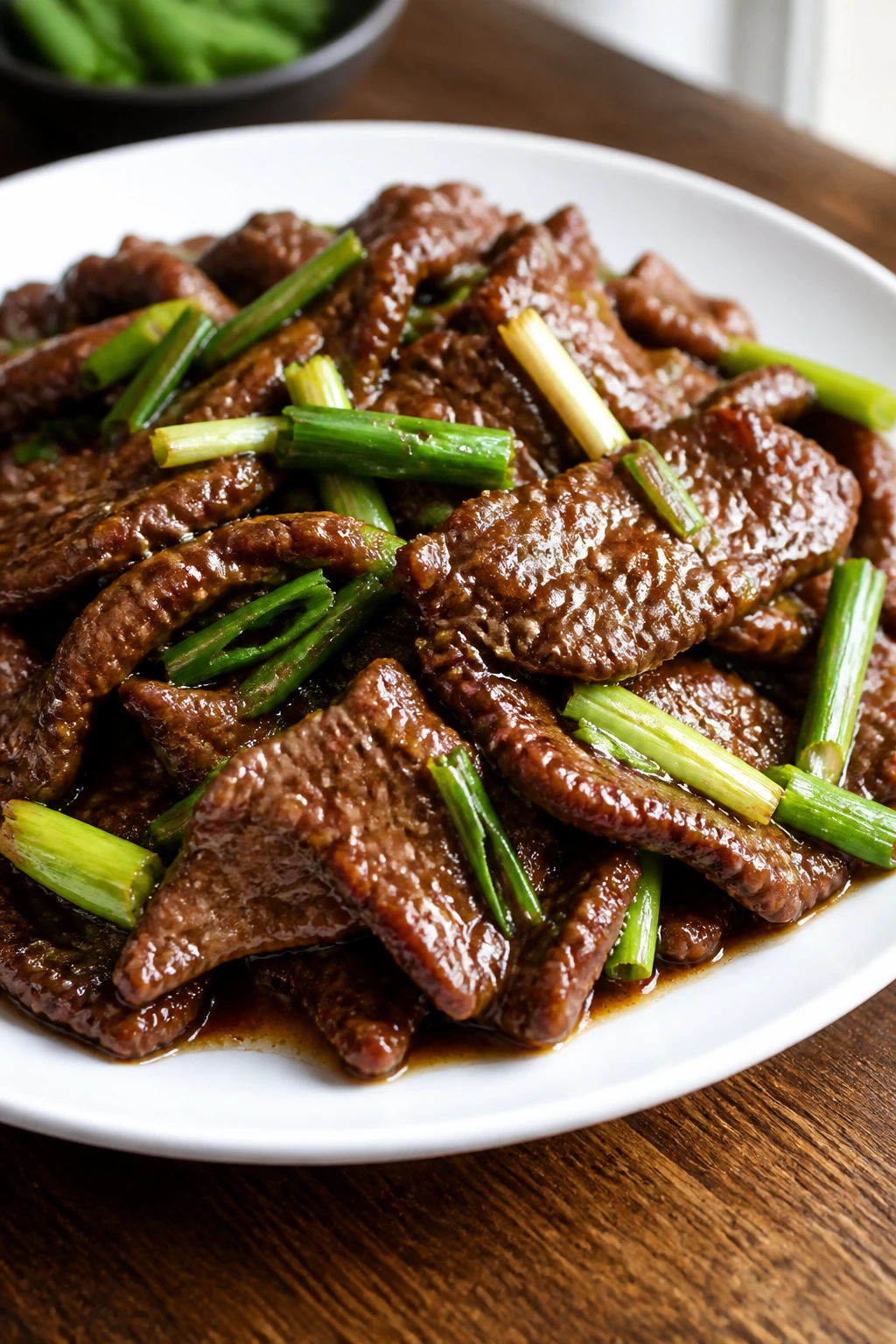 Close-up of glossy Mongolian beef with scallions on a plate in a warm kitchen.