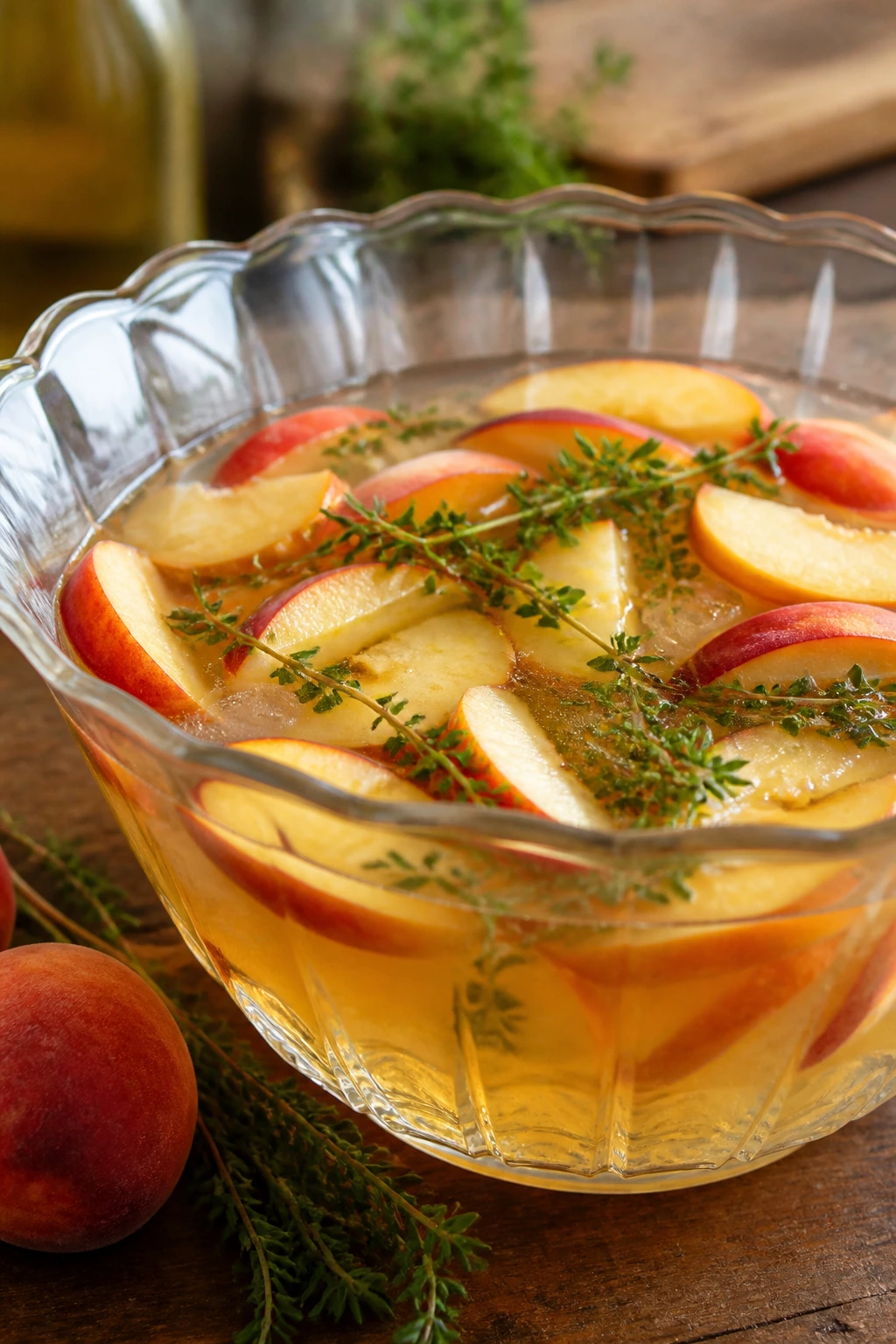 Close-up of Nectarine Thyme Sangria Punch in a glass bowl with nectarine slices and thyme on a rustic wooden counter