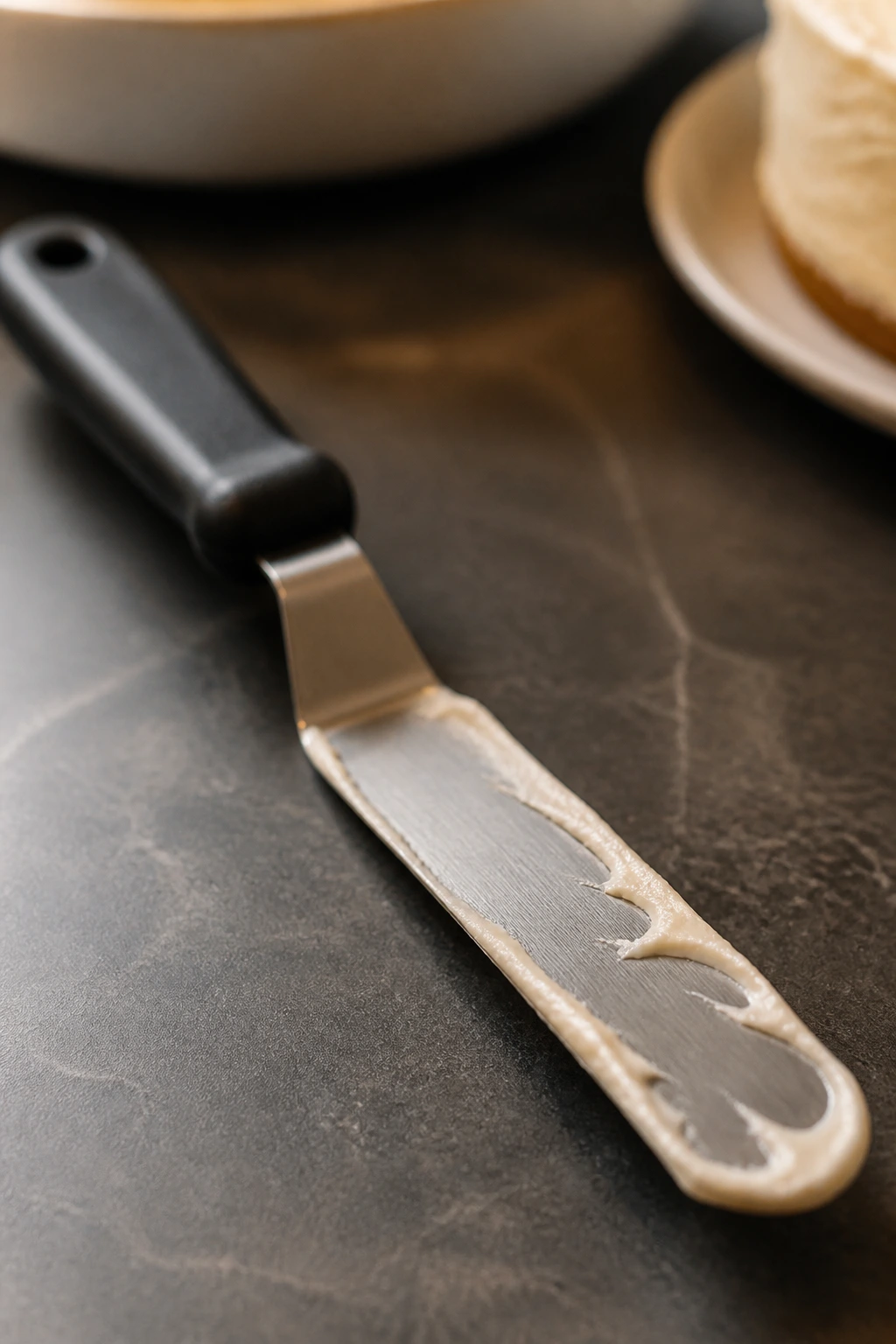 Offset spatula with frosting on blade on a dark countertop