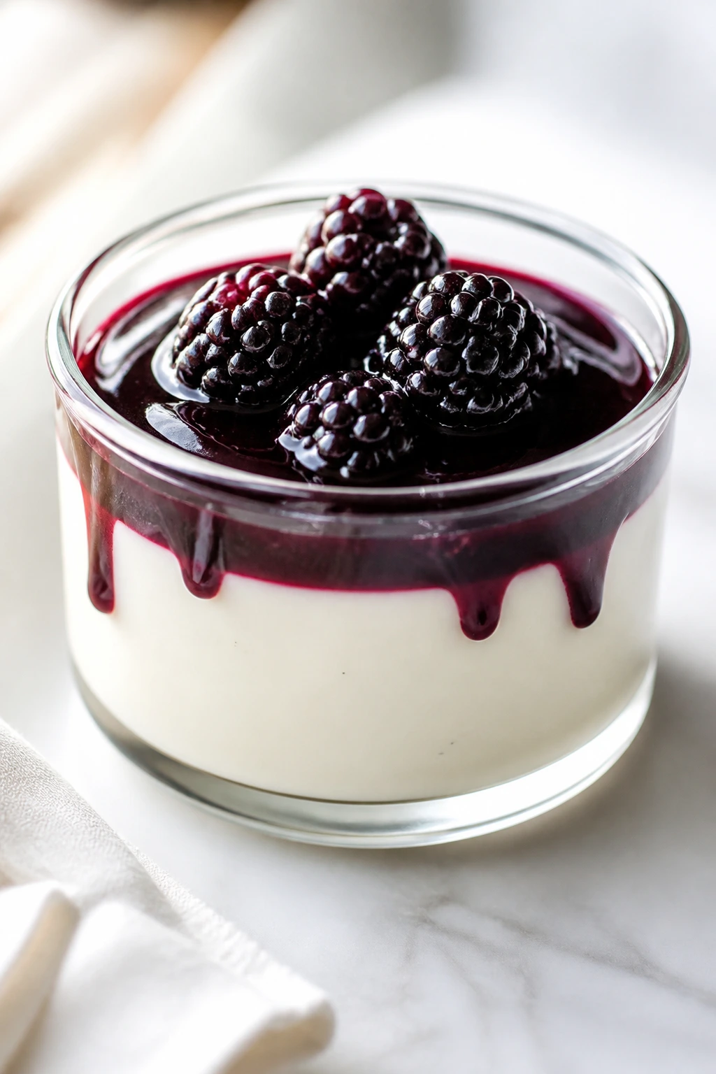 Vanilla panna cotta in ramekin with blackberry sauce.