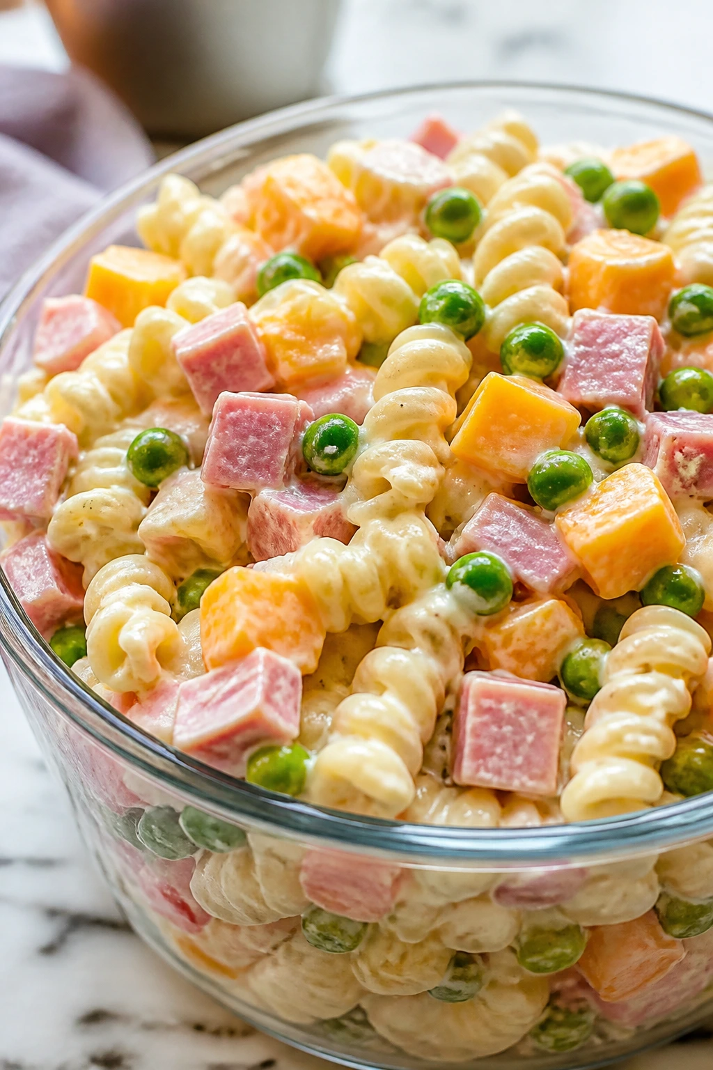 Pasta salad with ham, peas, and cheddar cubes in a clear bowl