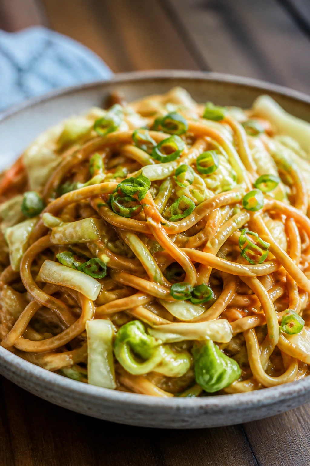 Close-up of peanut noodles with cabbage and scallions in a bowl.