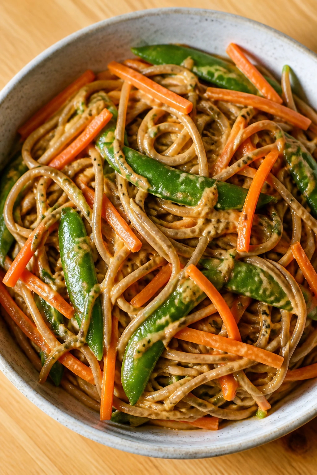 Close-up of peanut soba noodles with snap peas and carrots in a bowl