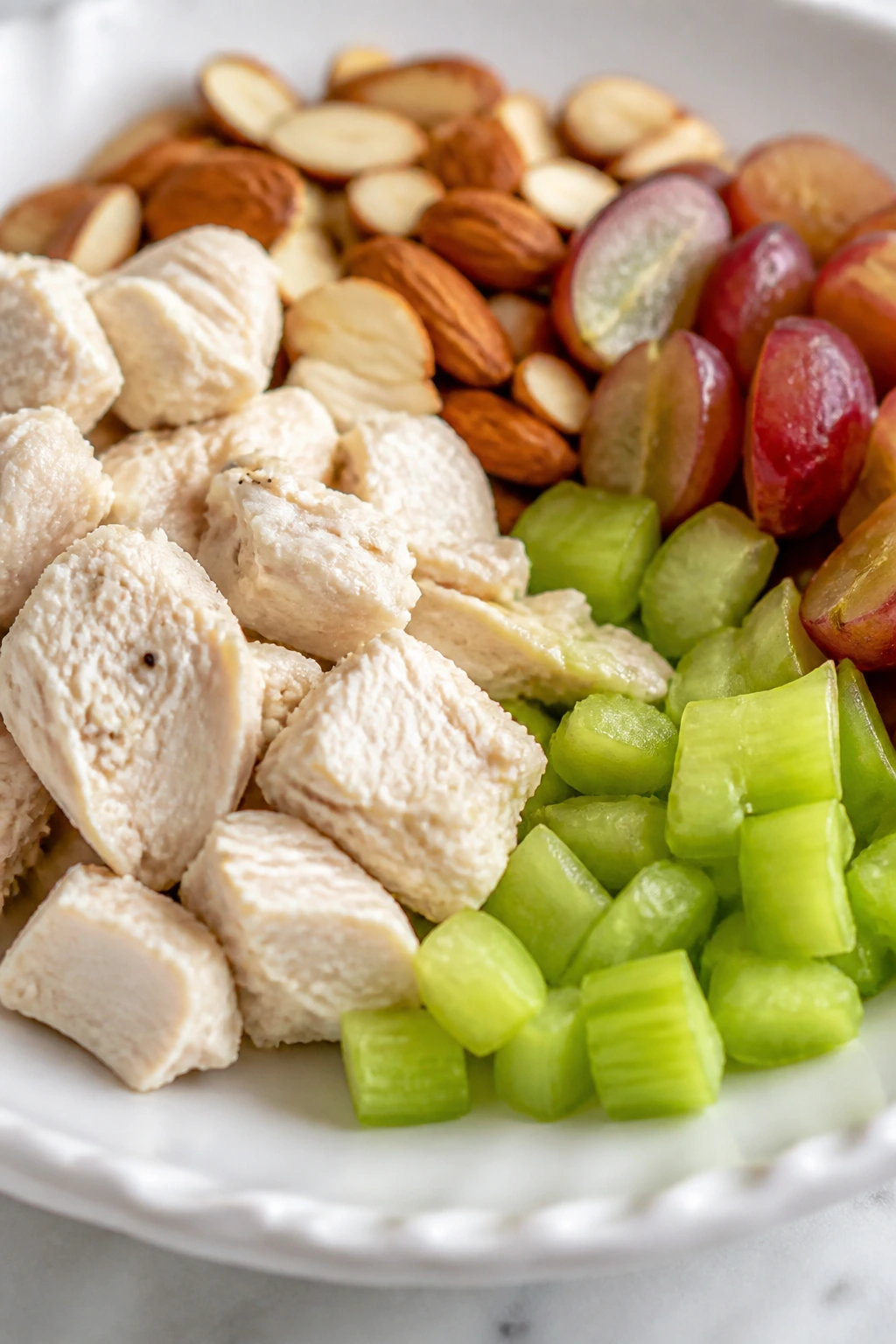 Close-up of poached chicken, celery, almonds, and grapes on a plate