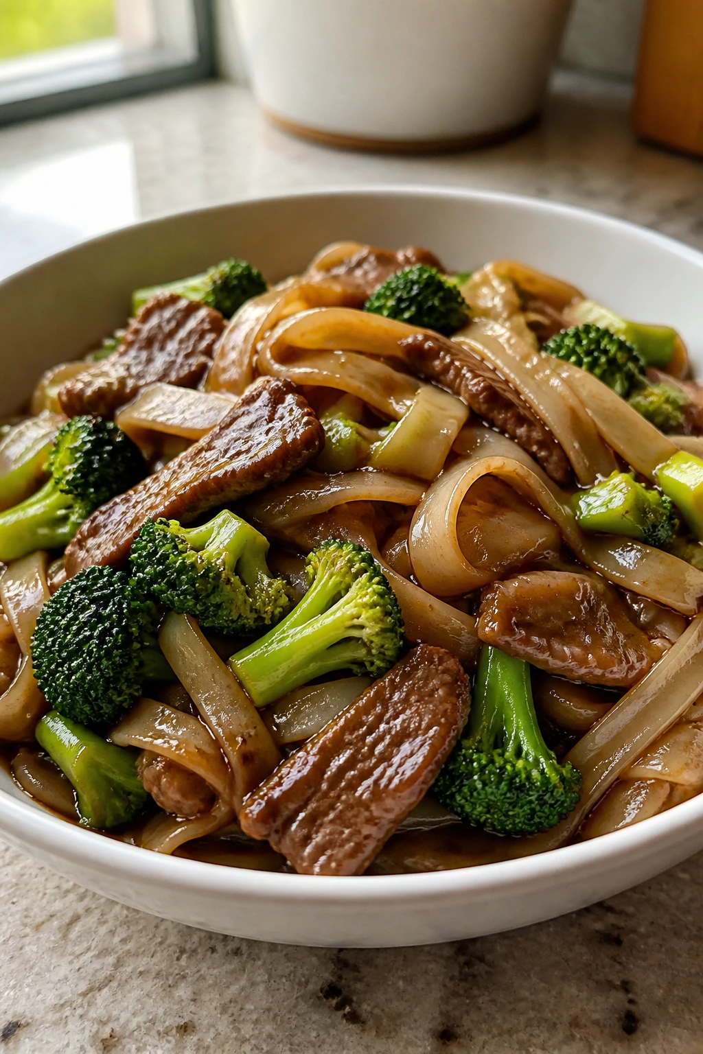 Beef and broccoli rice noodles in a glossy sauce in a bowl