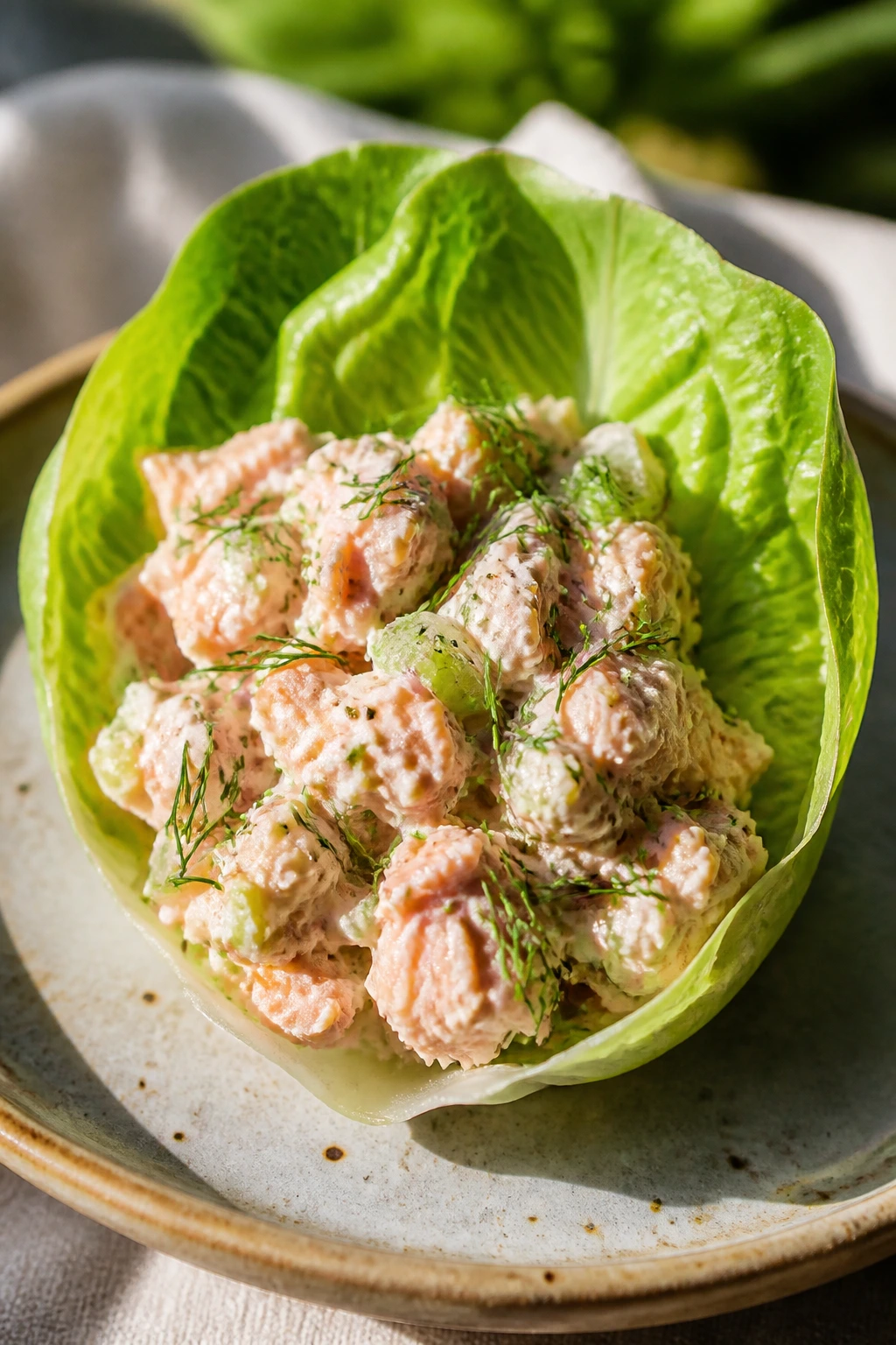 Lettuce cup filled with dill salmon salad on a rustic plate outdoors.