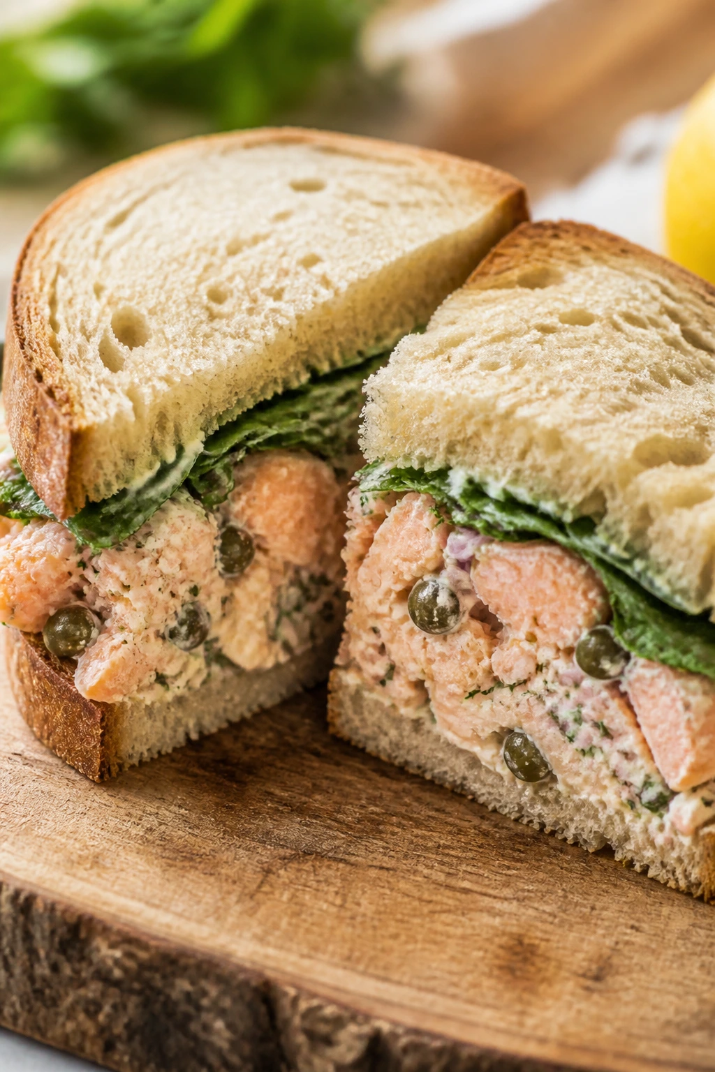 Close-up of salmon salad sandwich halves with capers on a rustic board